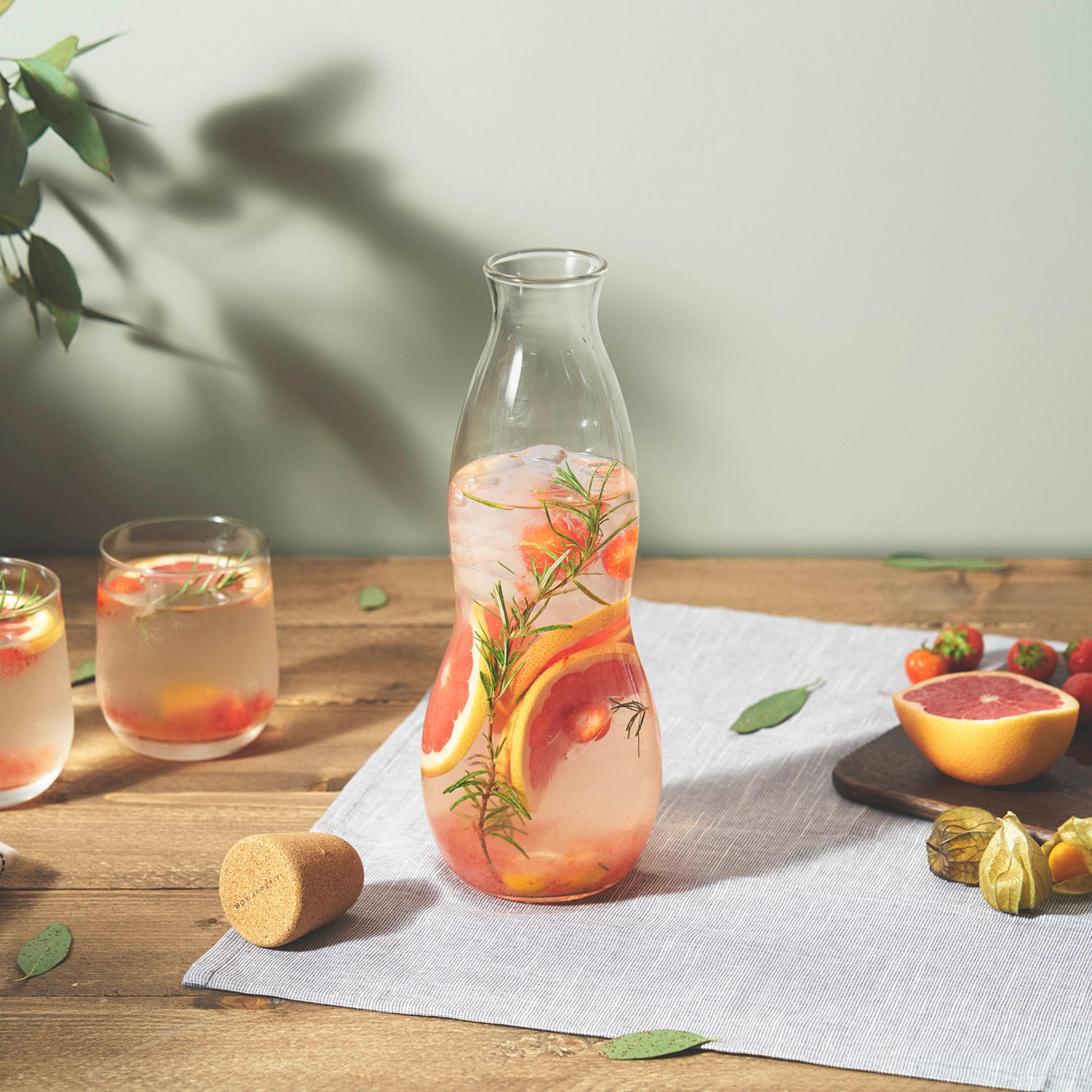 Glaswasserflasche mit Früchten und Eis. Zwei Gläser mit Getränk auf dem Holztisch. Weißer Hintergrund.