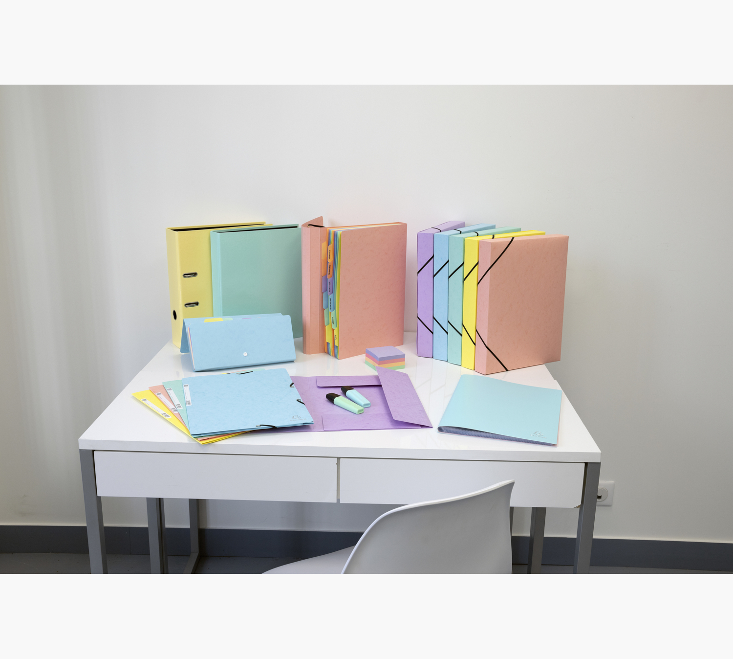 Białe biurko z kolorowymi teczkami, długopisami i karteczkami samoprzylepnymi.