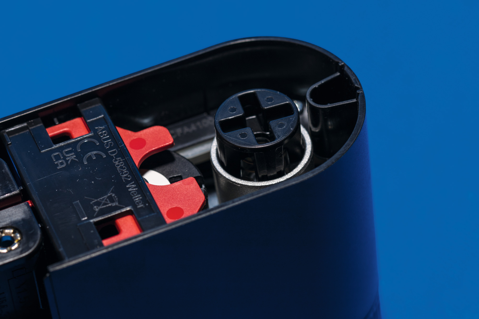 Wnętrze czarnego urządzenia z czerwonymi i czarnymi częściami, na niebieskim tle.