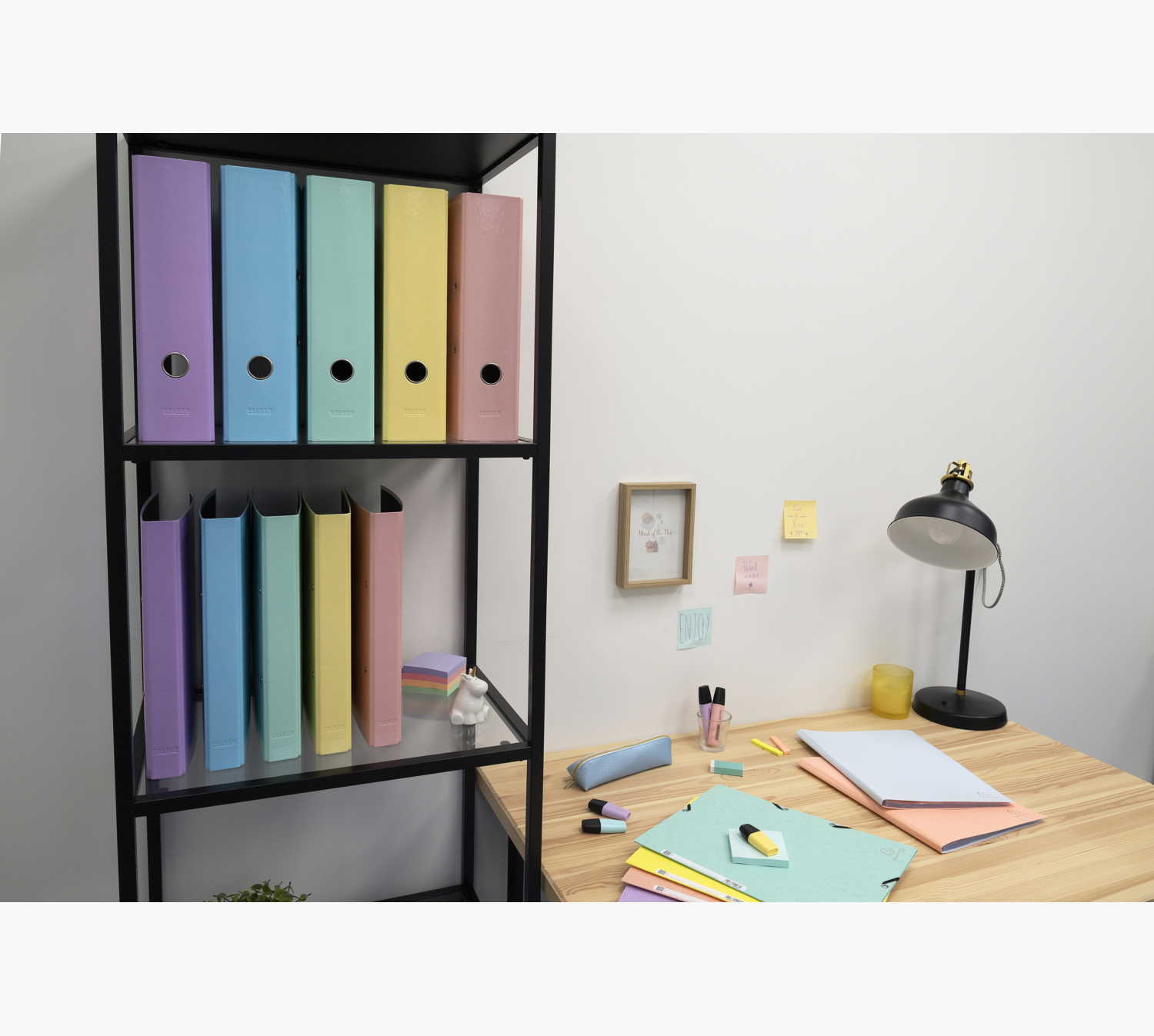 Biuro z kolorowymi segregatorami na półce. Biurko z artykułami piśmienniczymi i lampą.