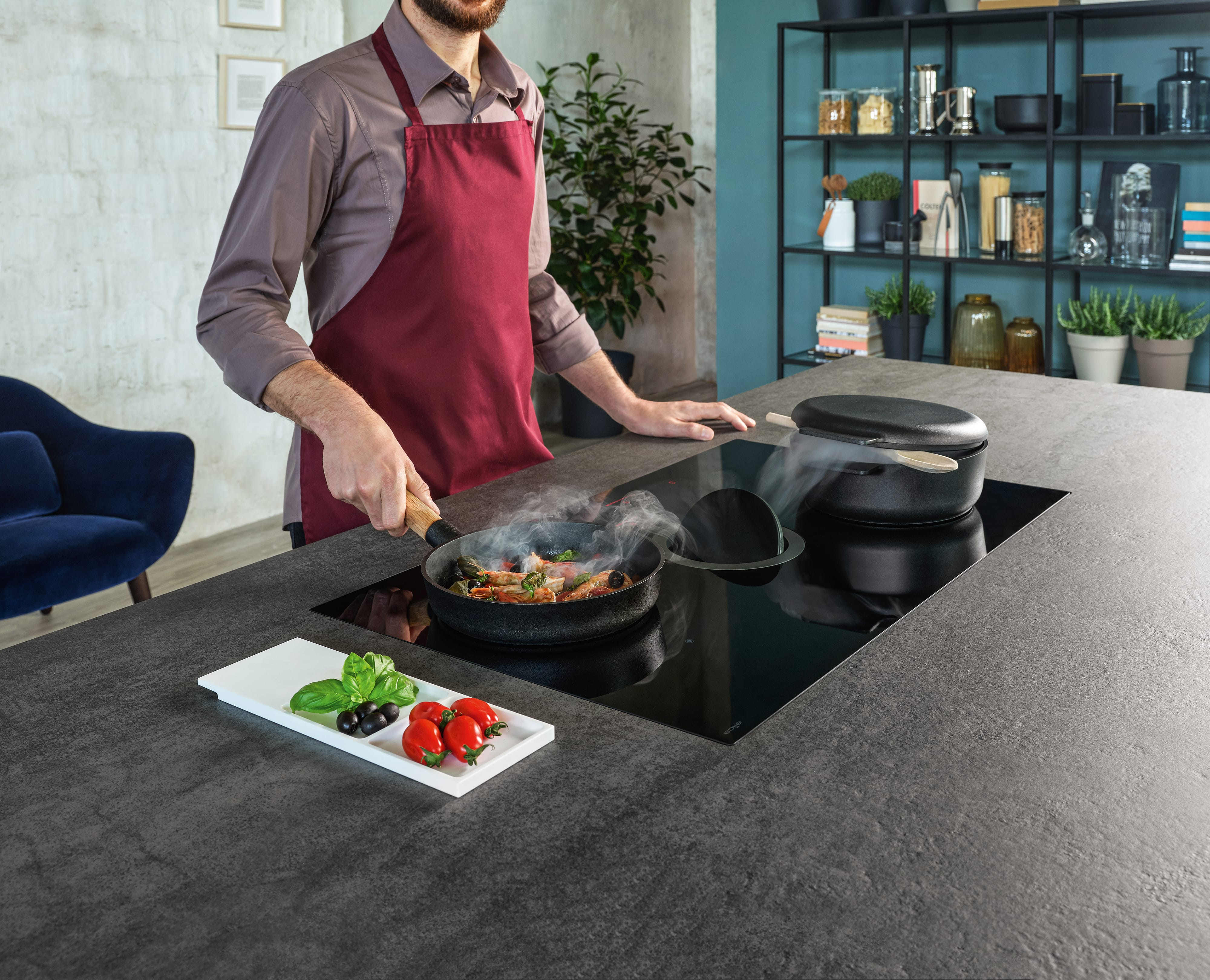 Una persona cucina su un piano cottura moderno con una padella, ingredienti e un aspiratore integrato.