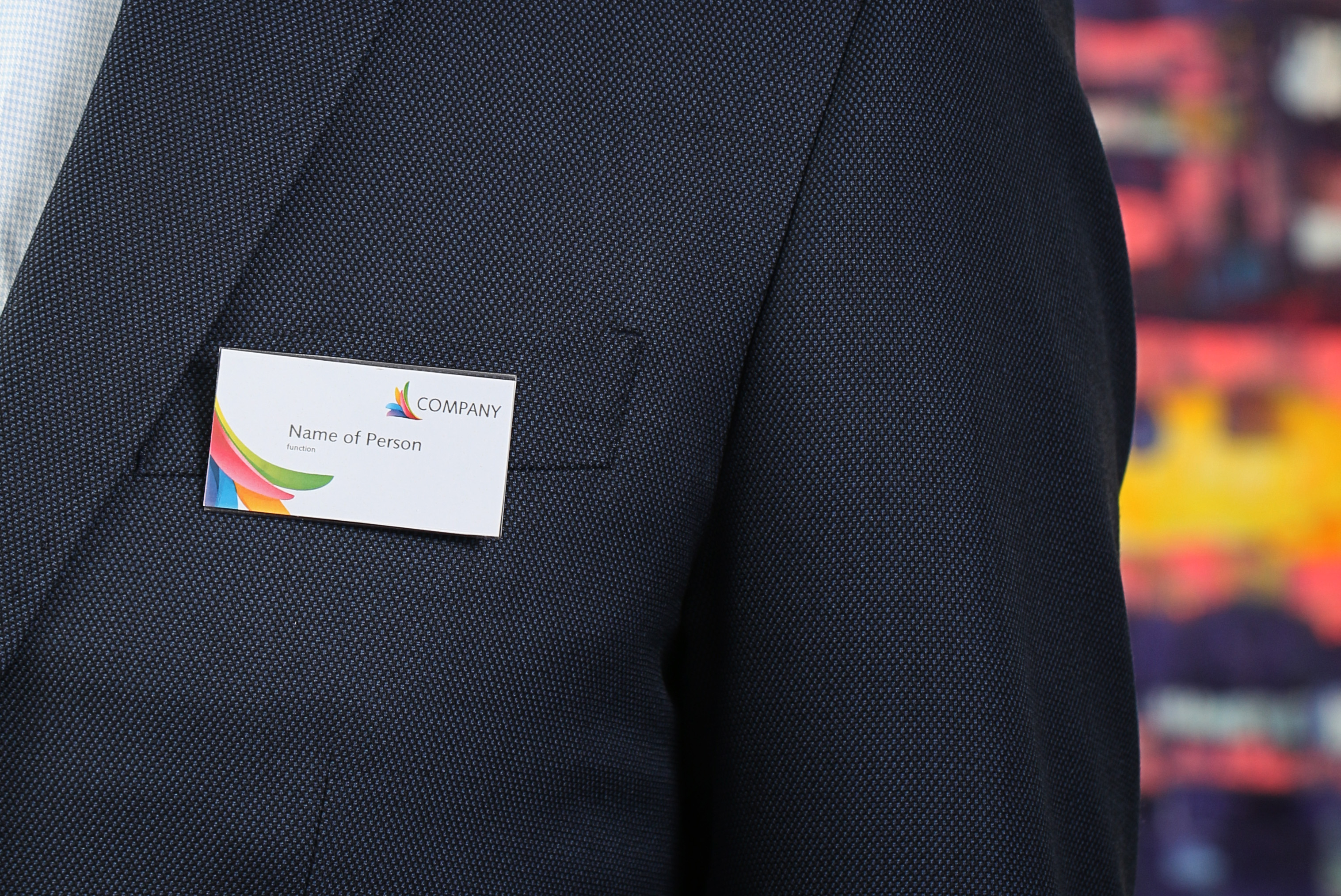 Osoba w ciemnym garniturze nosząca identyfikator. Identyfikator wyświetla logo firmy i imię.