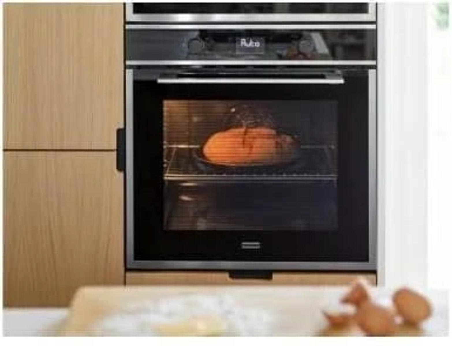 Un forno con una pagnotta di pane all'interno. C'è un tagliere di legno in primo piano.