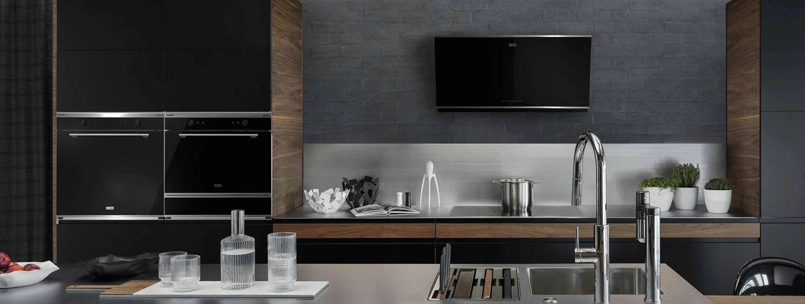 Siyah dolaplar, ahşap vurgular ve paslanmaz çelik tezgahlı modern mutfak. Bir lavabo ve fırın.
