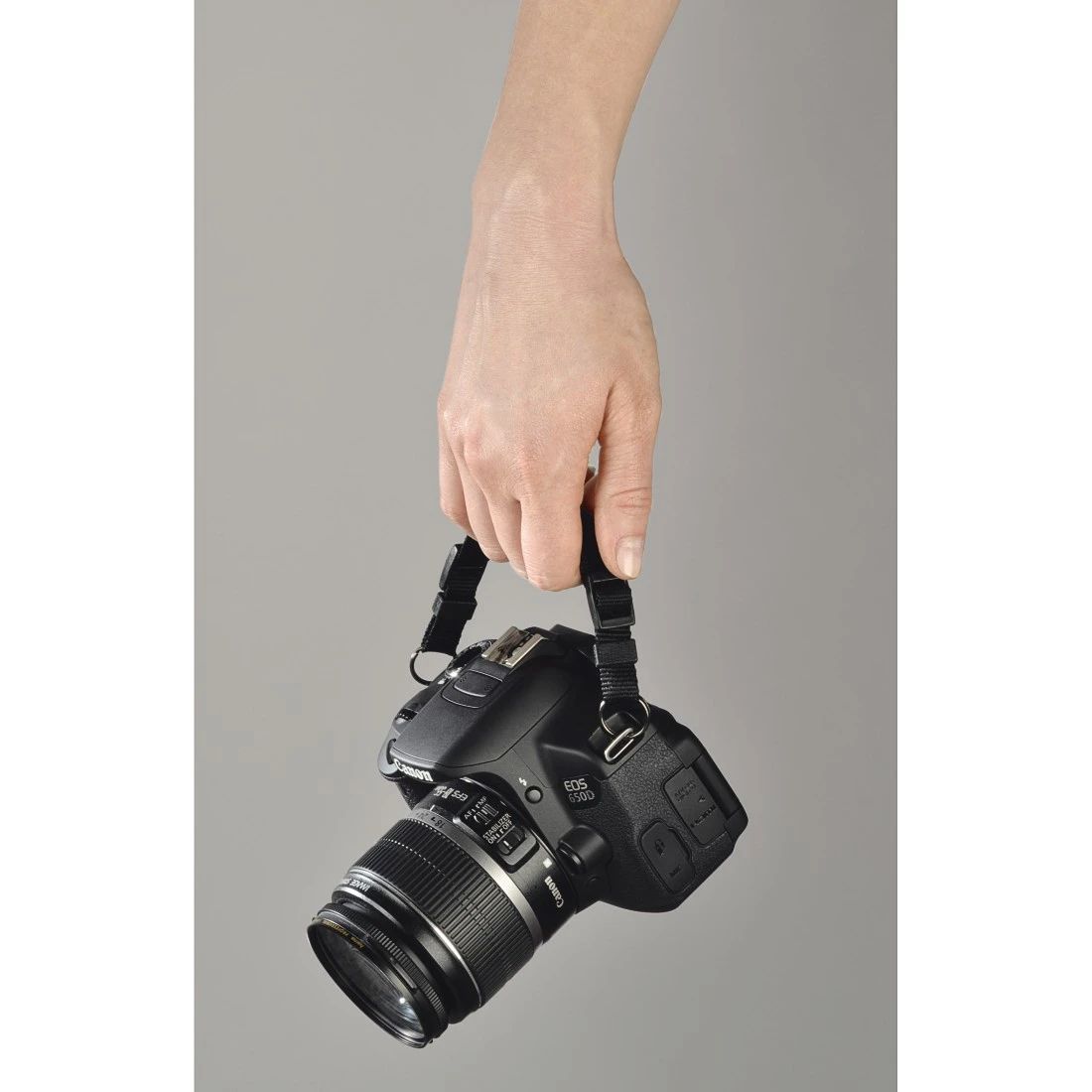 Una mano che tiene una fotocamera Canon nera con un obiettivo. Lo sfondo è grigio.