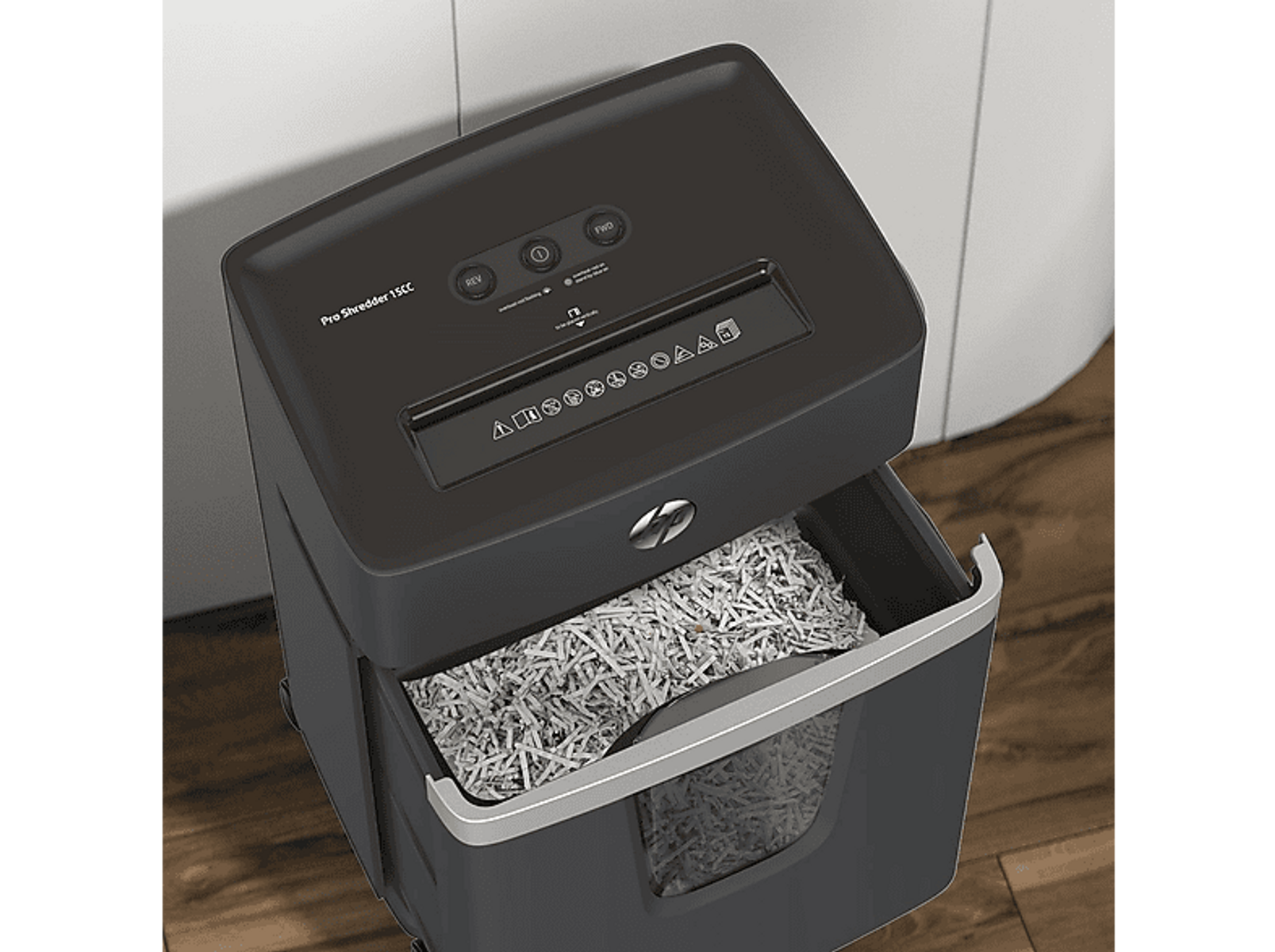 Czarna niszczarka do papieru z otwartym pojemnikiem wypełnionym pociętym papierem. Szary element na białym i drewnianym tle.