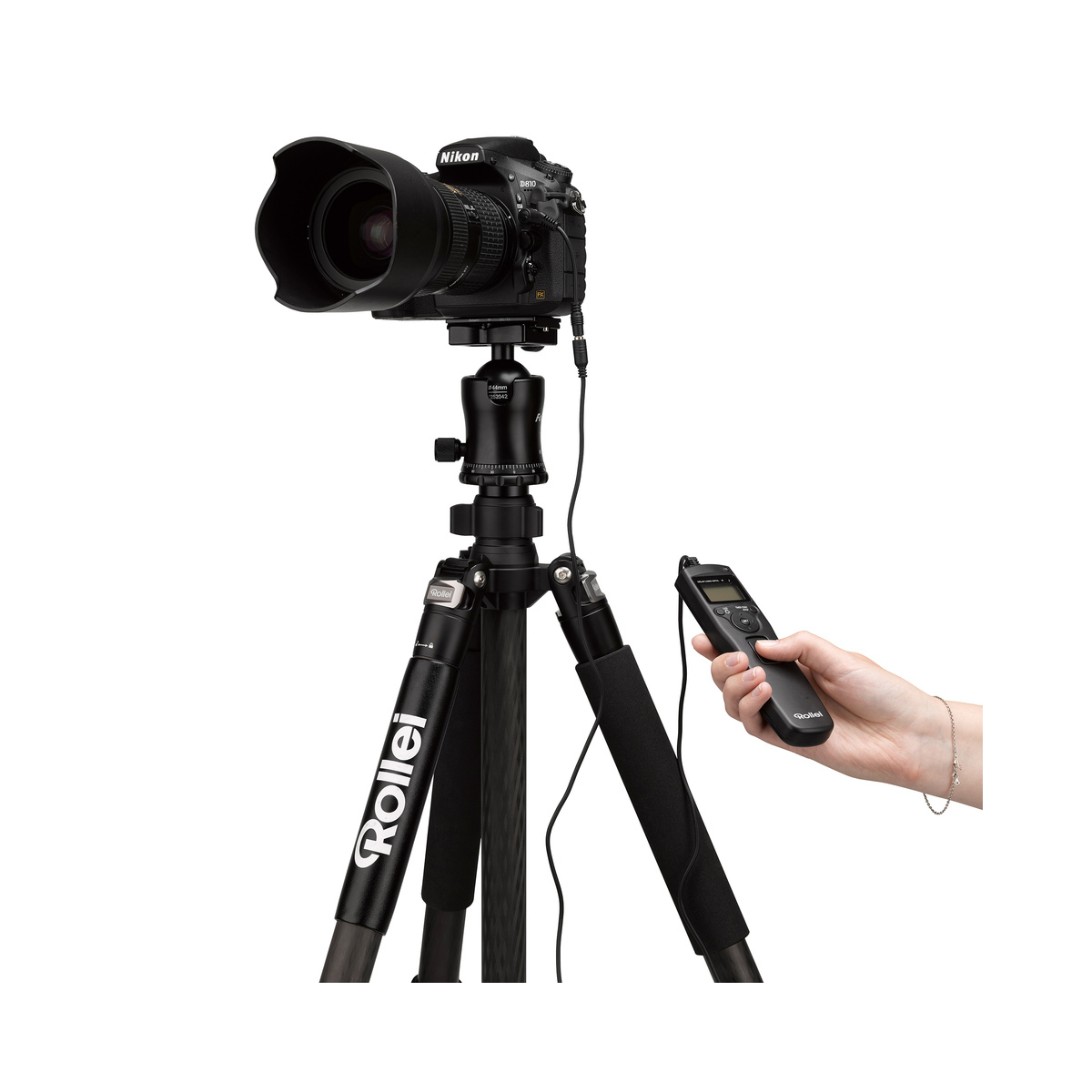 Aparat na statywie z pilotem w dłoni. Białe tło.