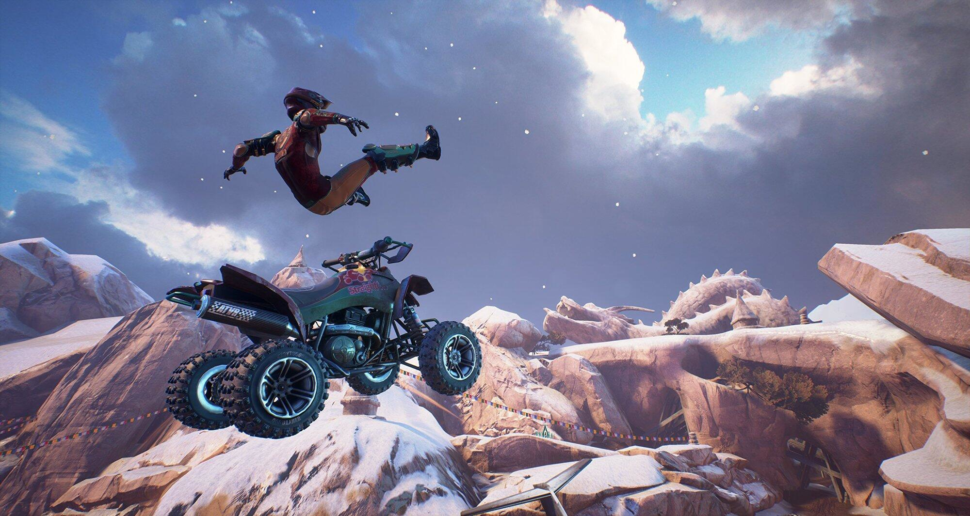 Una persona su un ATV salta in aria. Lo sfondo è un terreno montuoso innevato.