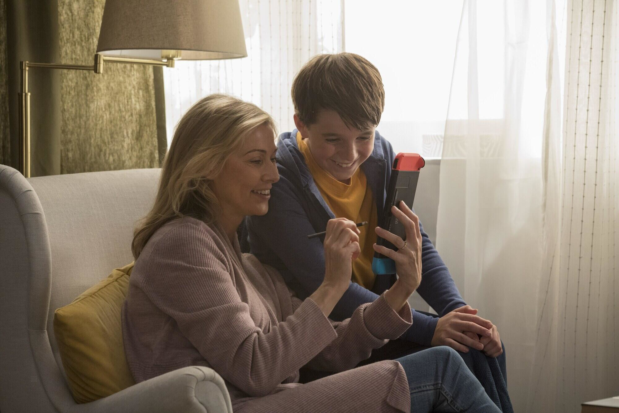 Matka i syn patrzą na konsolę, uśmiechają się i cieszą się grą.