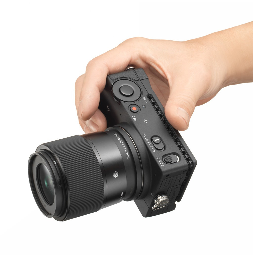 Dłoń trzymająca czarny aparat z obiektywem, skierowany w stronę widza.