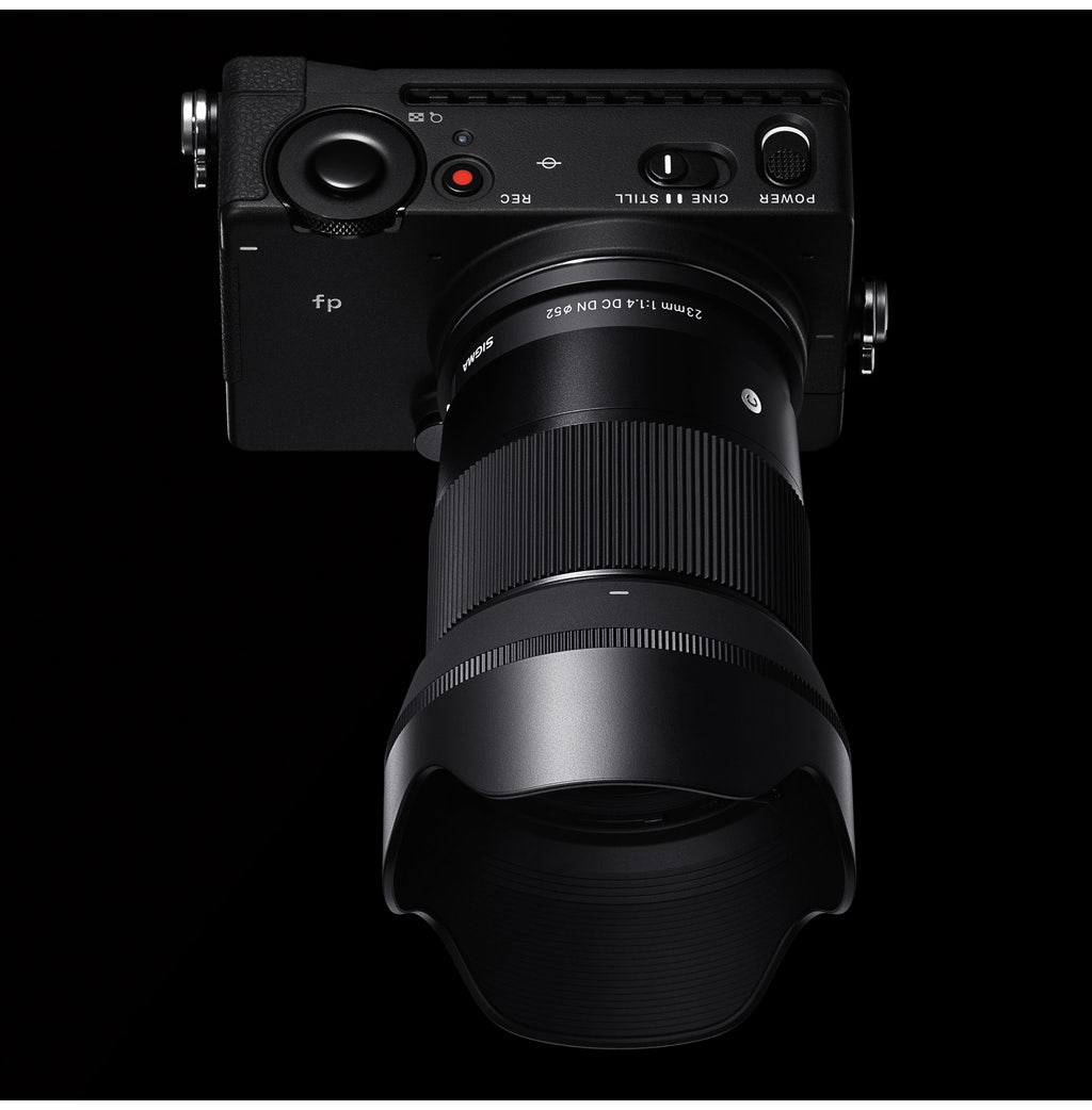 Czarny aparat z obiektywem, obiektyw skierowany w stronę widza na czarnym tle.