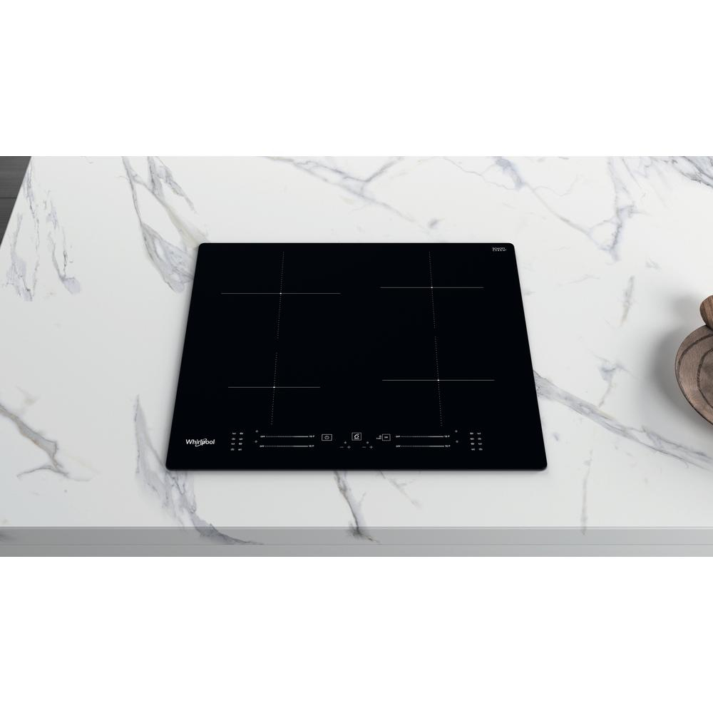 Placa de cocina negra sobre encimera de mármol blanco, cuatro quemadores, desde un ángulo.
