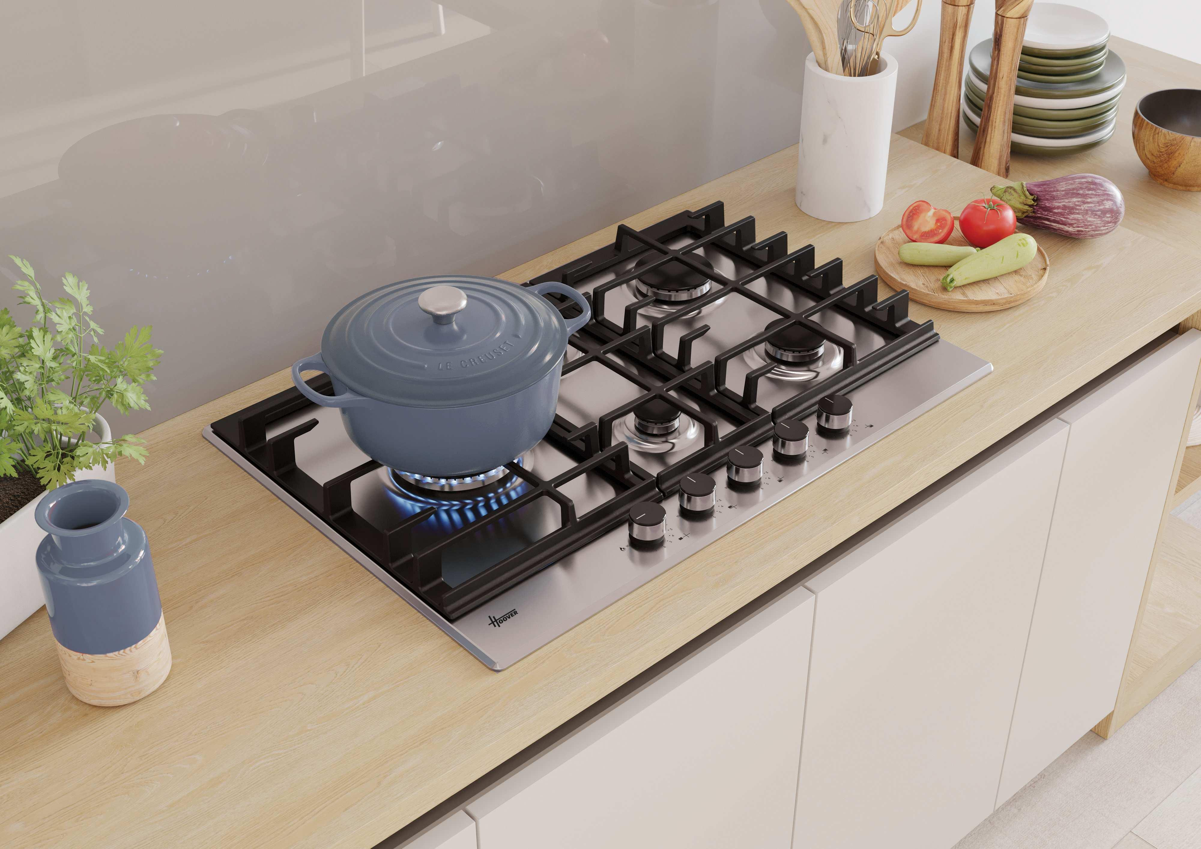 Cucina con piano cottura, pentola blu sul fuoco, piano in legno e verdure.