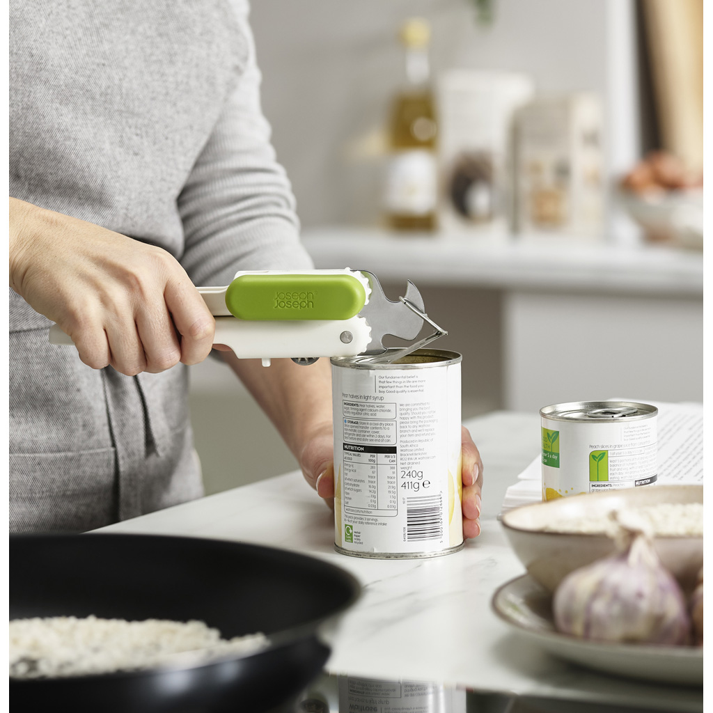 Una persona usando un abrelatas blanco y verde para abrir una lata de comida. Hay otras latas y alimentos presentes.