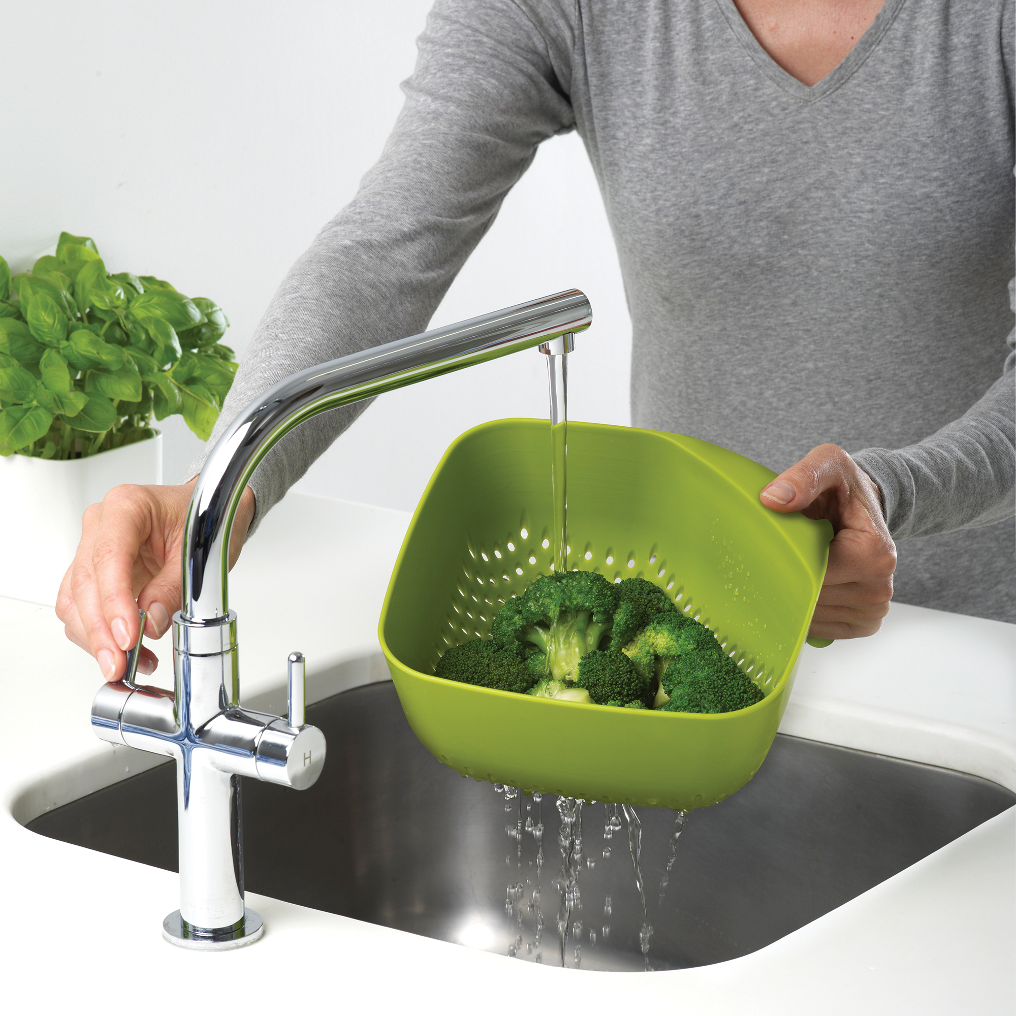 Brócoli lavándose en un escurridor verde bajo un grifo cromado en un fregadero de acero inoxidable.