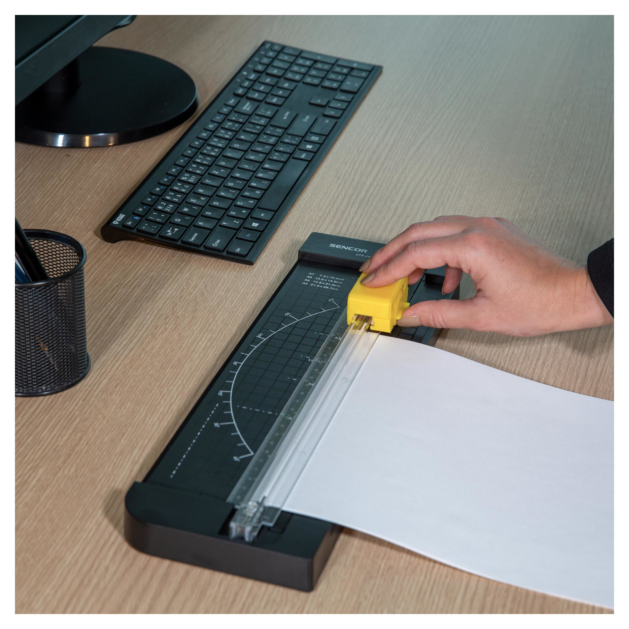 Osoba używa gilotyny do papieru. Klawiatura i monitor są w tle.