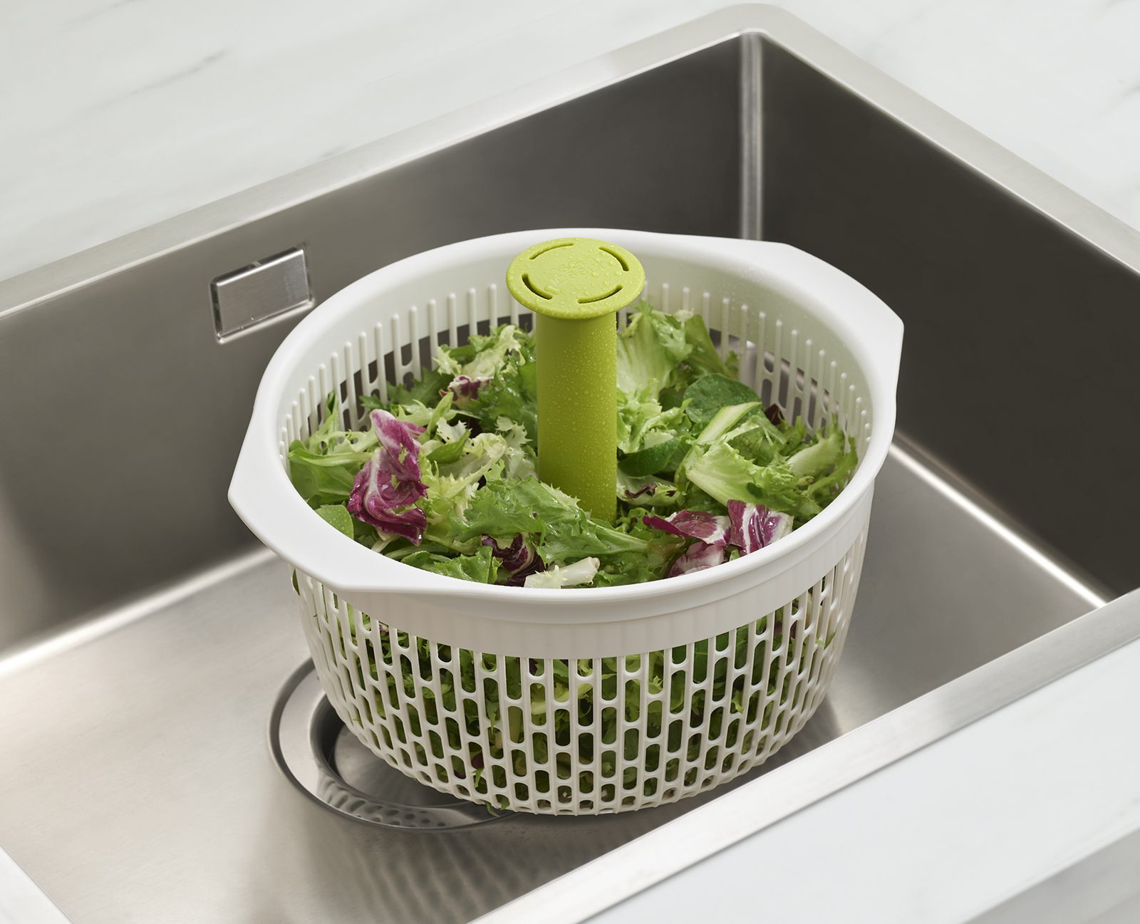 Eine Salatschleuder mit Salat darin, in ein Waschbecken gestellt.