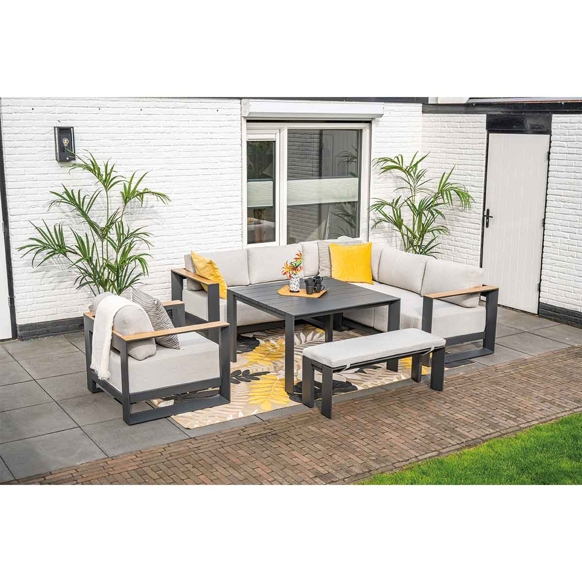 Buitenzithoek met hoekbank, tafel, bank en planten. Witte bakstenen muur.