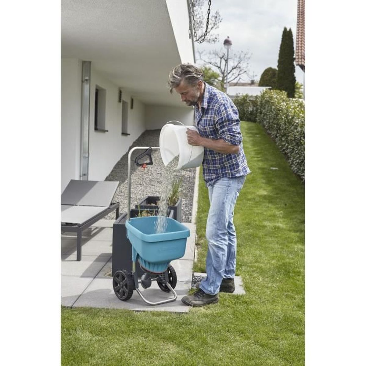Ein Mann befüllt einen teal-farbenen und schwarzen Gartenspreizer mit einem weißen Eimer.