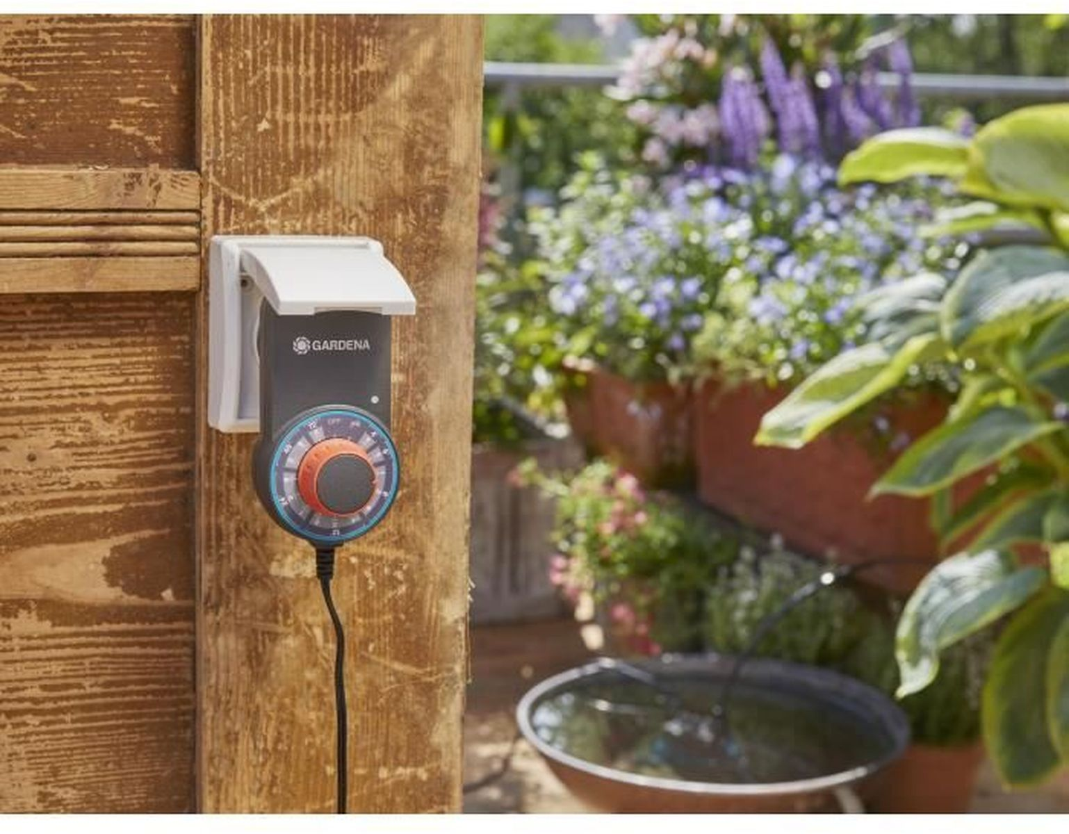 Ein Gartentimer an einer Holztür befestigt. Eine Wasserquelle ist im Hintergrund sichtbar.