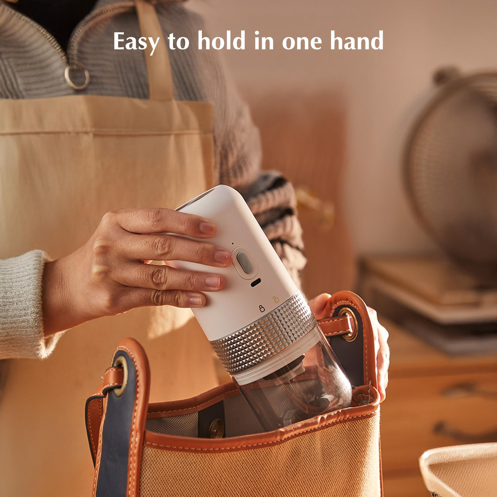 Eine Frau legt einen weißen und silbernen Kaffeemühle in eine Handtasche. Beiger Hintergrund.