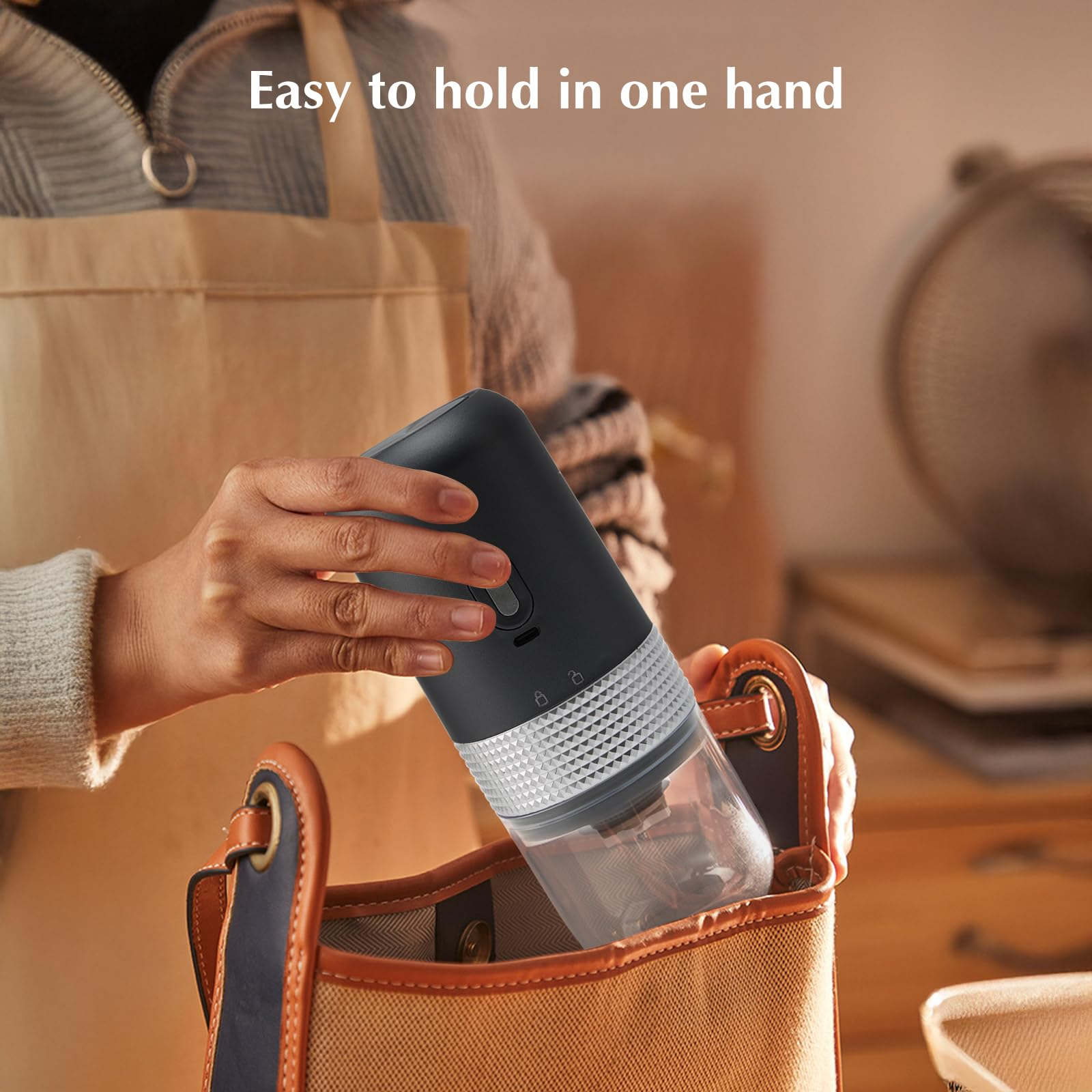 Eine Person hält eine schwarze, tragbare Kaffeemühle und legt sie in eine braune Tragetasche.