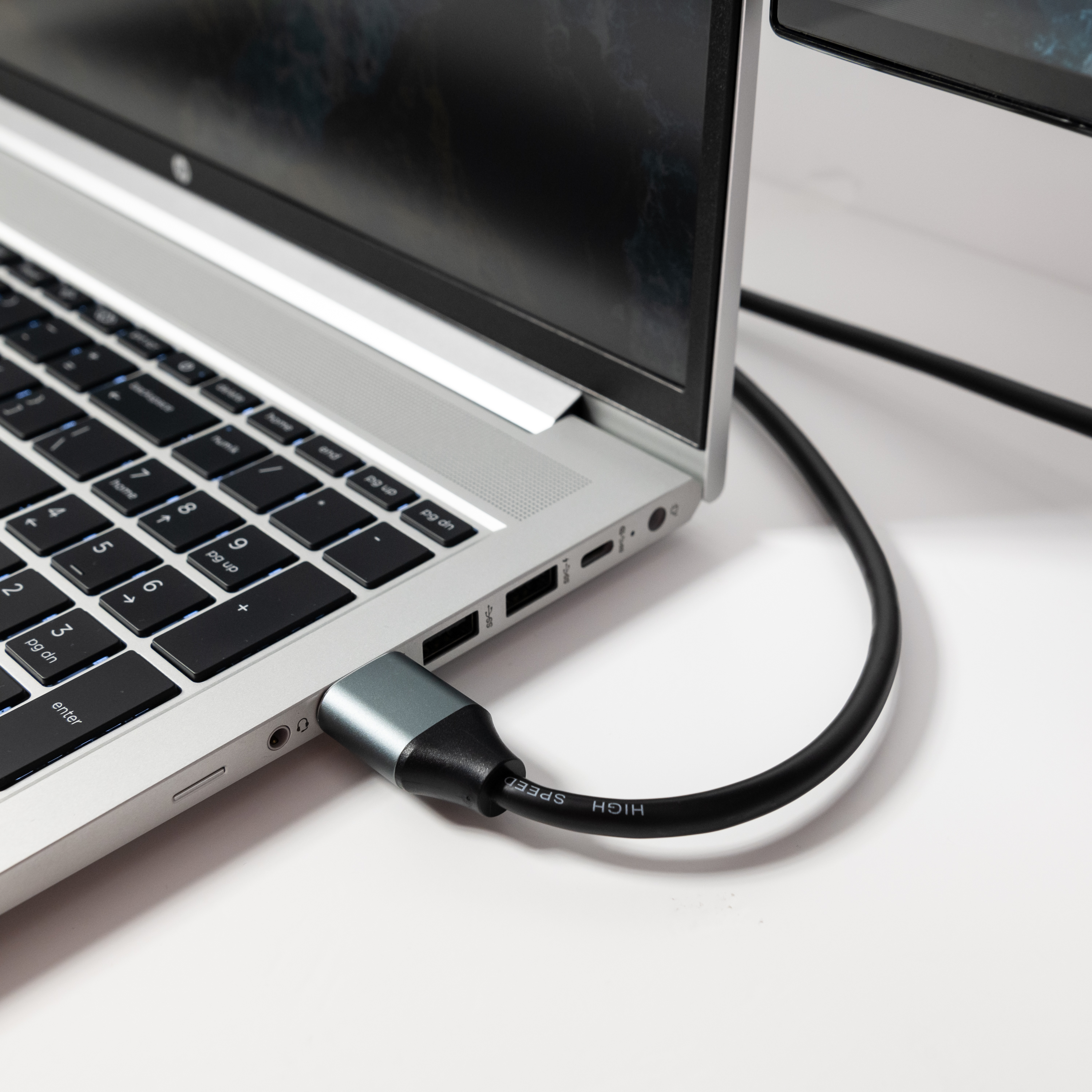 Srebrny laptop z podłączonym kablem HDMI, białe tło.