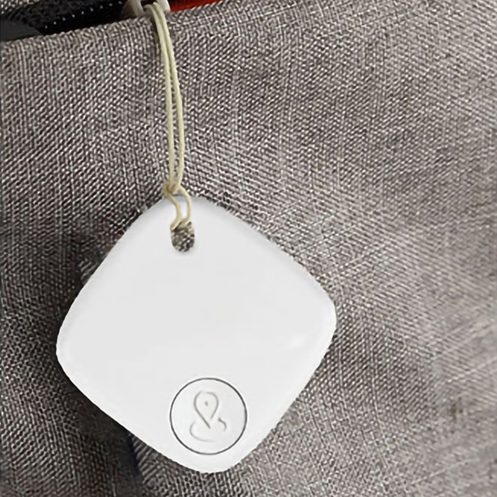 Tracker quadrato bianco attaccato a tessuto grigio. Ha un pulsante e un'icona di posizione.