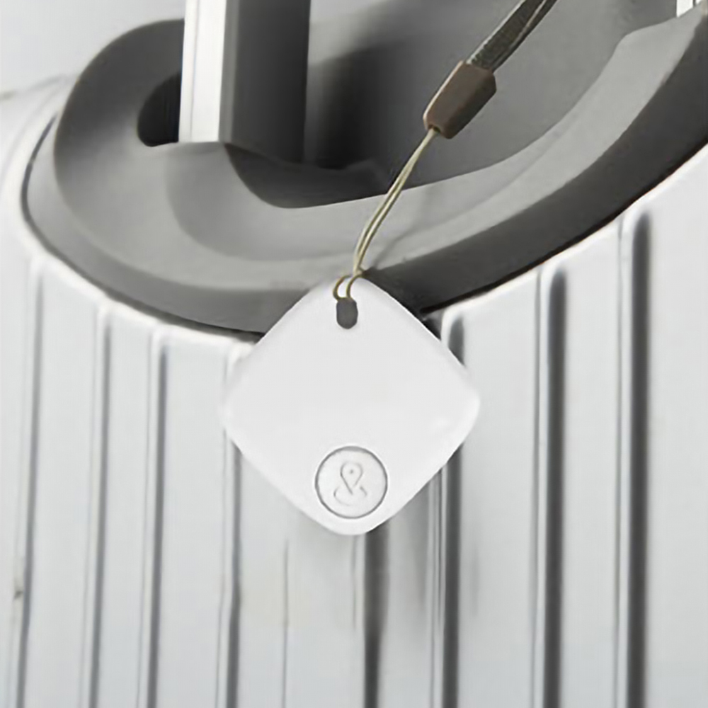 Un dispositivo quadrato bianco con un logo e un cordino, probabilmente un tracker, su una valigia grigio chiaro.