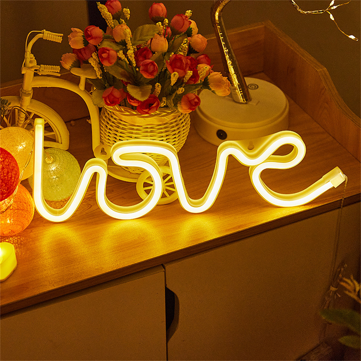 Eine Holzoberfläche mit einem beleuchteten 'love'-Schild, Blumen in einem Korb und Lichtern.