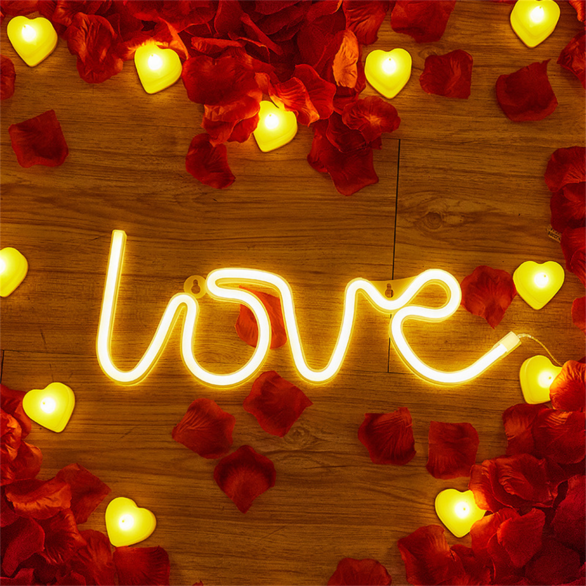 Ein beleuchtetes 'love'-Schild, umgeben von roten Rosenblättern und herzförmigen Kerzen.