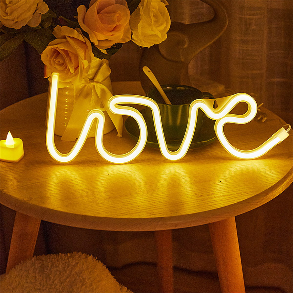 Ein Holztisch mit einem beleuchteten 'love'-Neonzeichen, Blumen und einer grünen Tasse.