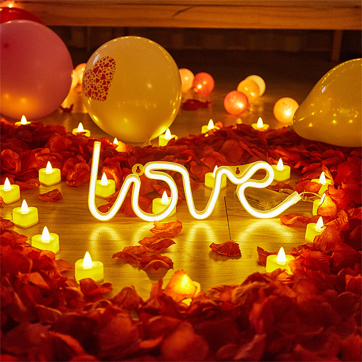 Ein beleuchtetes 'love'-Schild, umgeben von Rosenblättern, Kerzen und Luftballons.