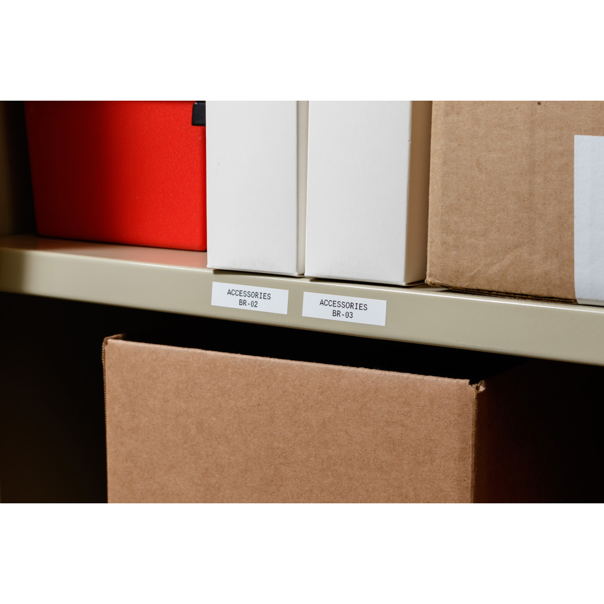 Białe etykiety z czarnym tekstem na metalowej półce. Widoczne są również pudełka i czerwony pojemnik.
