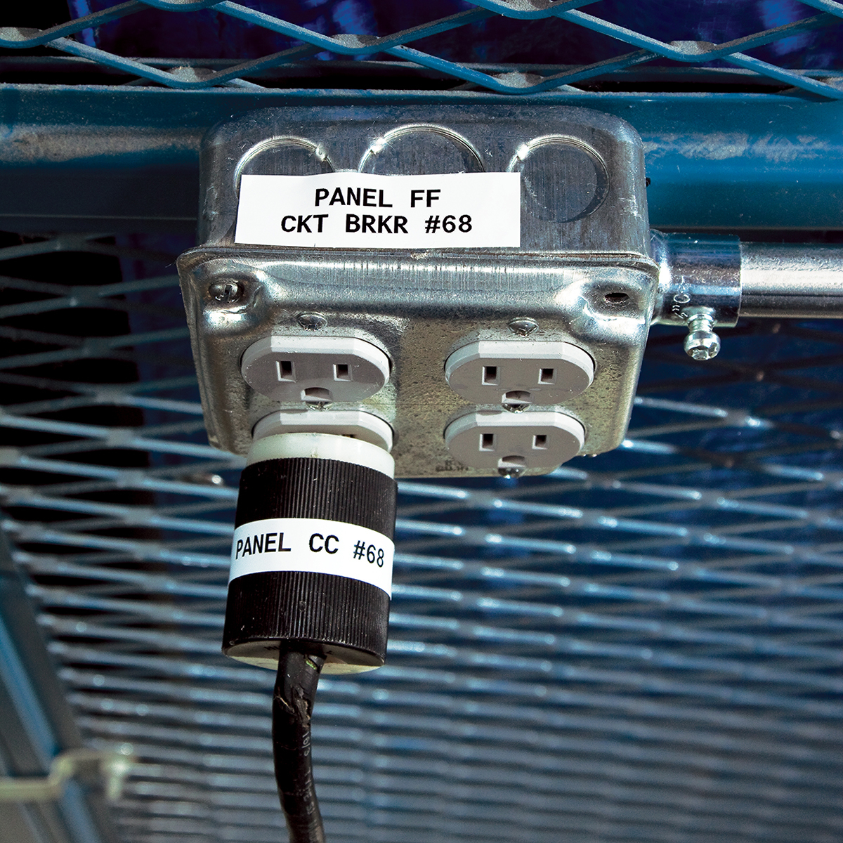 Metalowa skrzynka elektryczna z etykietami. Czarna wtyczka jest włożona od dołu.