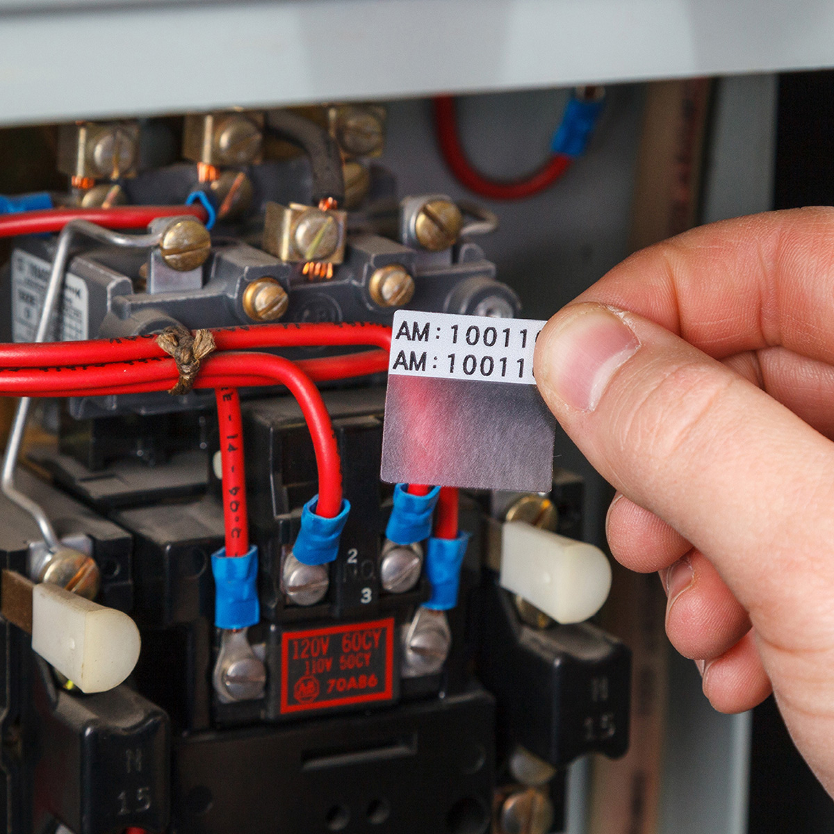 Ręka trzymająca etykietę z tekstem obok elementów elektrycznych.