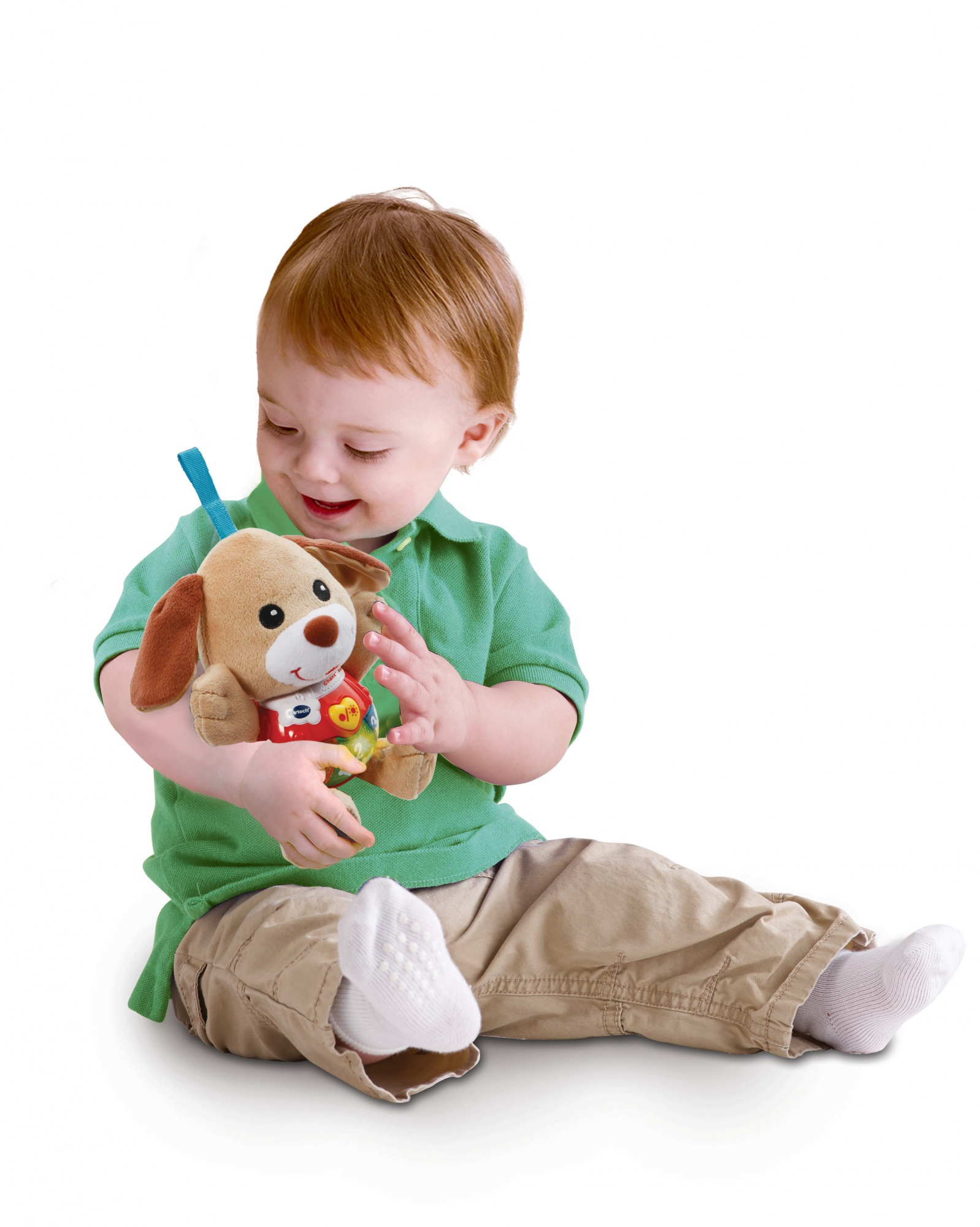 Ein Baby sitzt und hält ein Welpenspielzeug. Das Baby trägt ein grünes Hemd und khakifarbene Hosen.