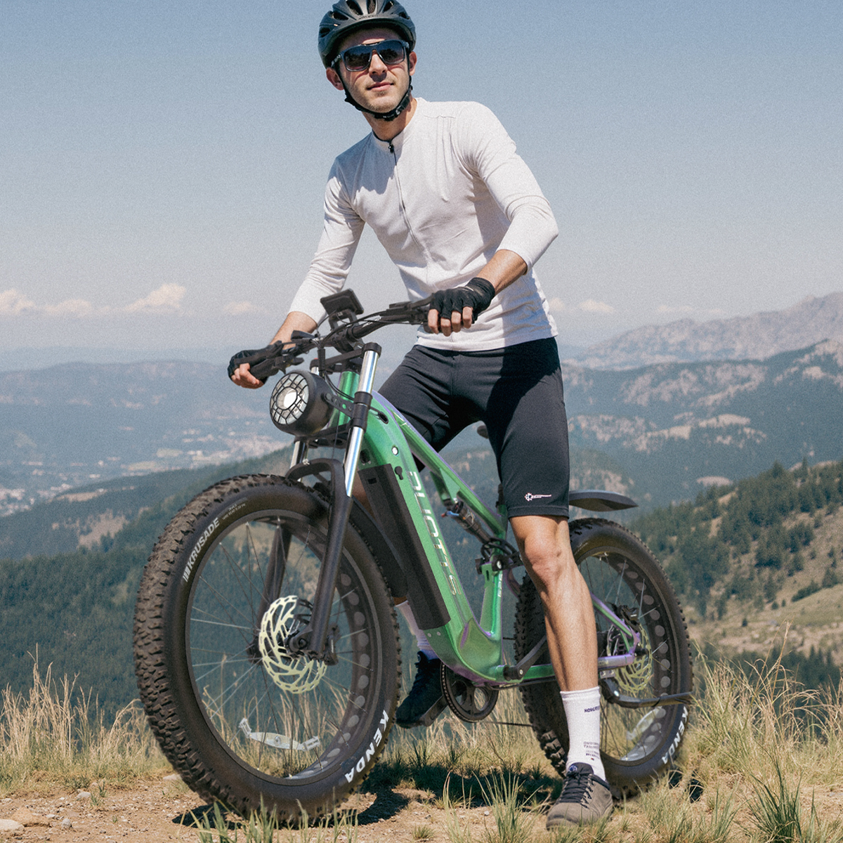 Mężczyzna na zielonym rowerze górskim, w kasku i okularach przeciwsłonecznych.