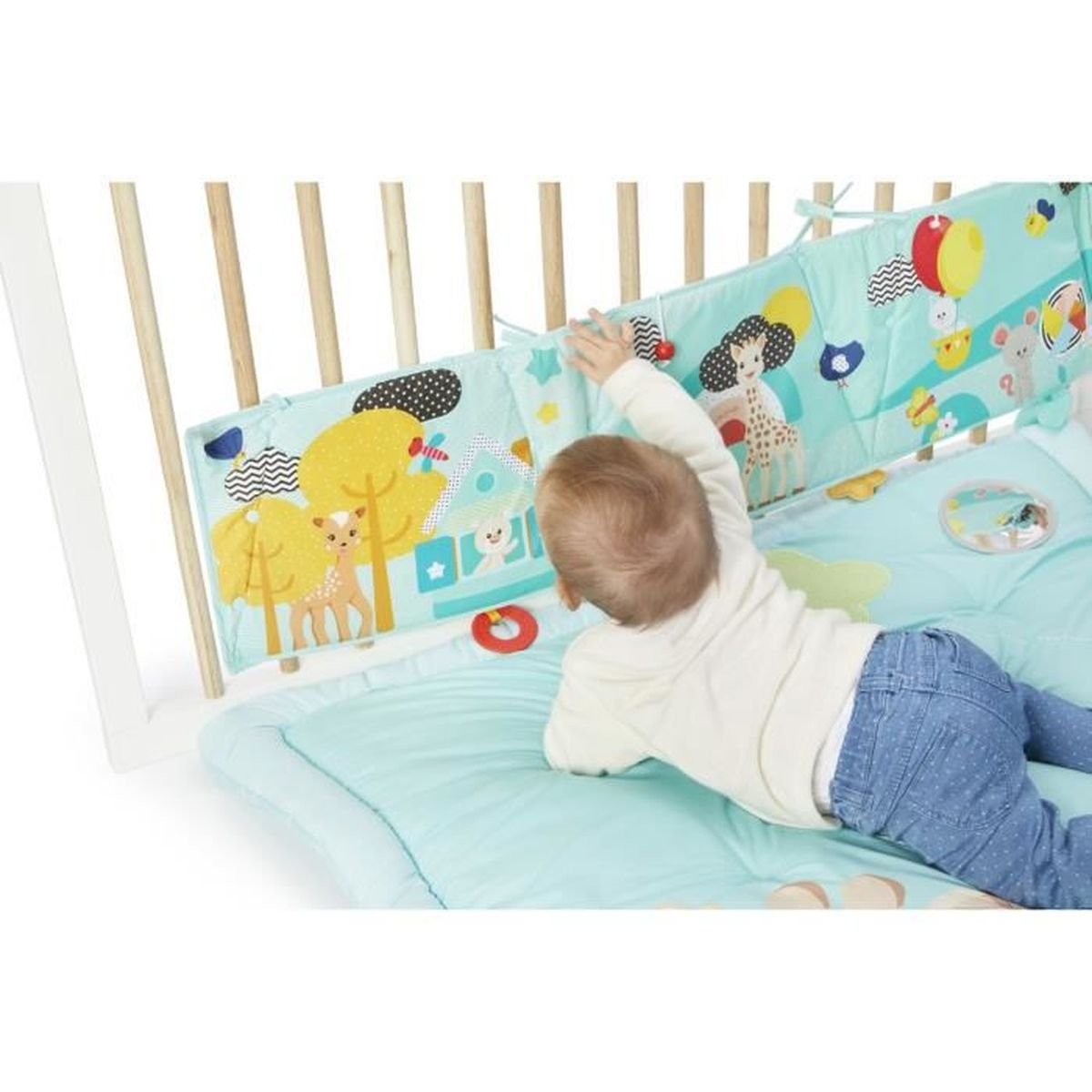Ein Baby liegt auf einer Spielmatte. Ein farbenfrohes Spielzeug ist am Kinderbett befestigt. Giraffen und Bäume sind abgebildet.