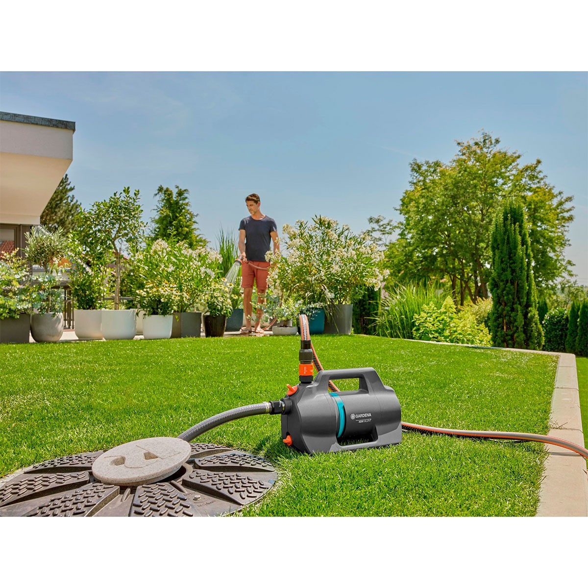 Mężczyzna podlewa rośliny wężem.  Pompa wodna stoi na trawie.