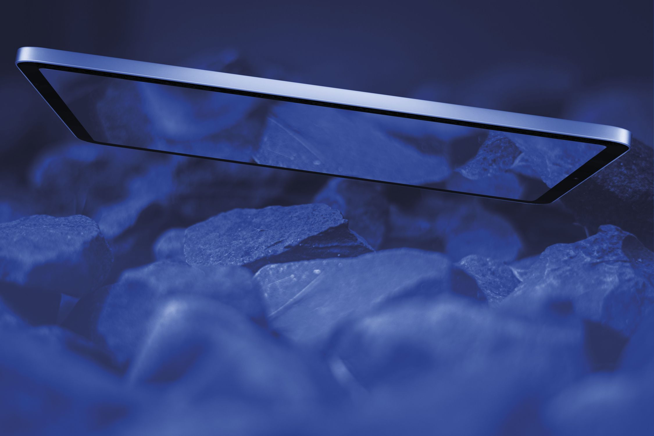 Imagen en tonos azules de una tableta sobre rocas azules oscuras.