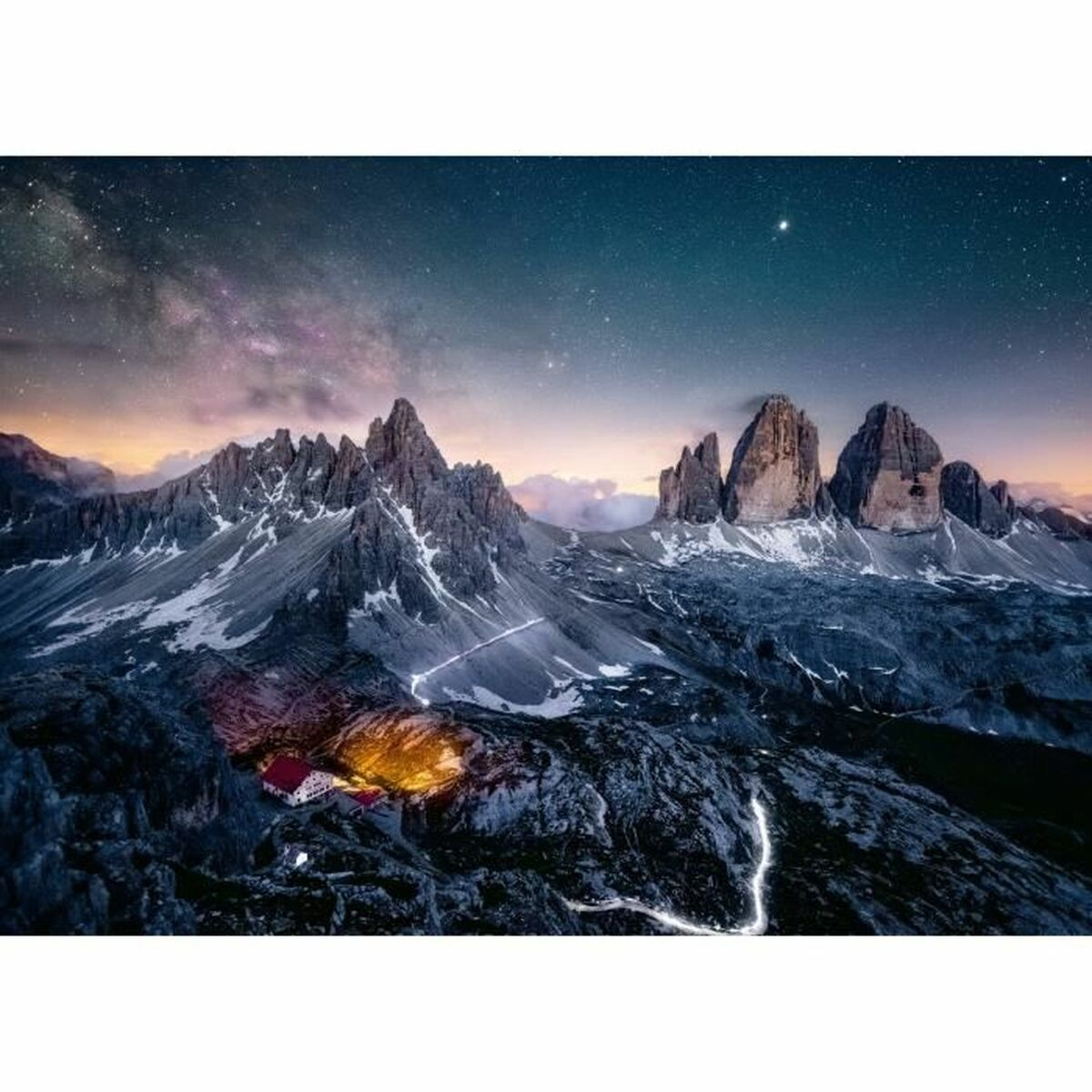 Un paysage de montagnes et un ciel étoilé la nuit. Il y a une cabane avec des lumières.