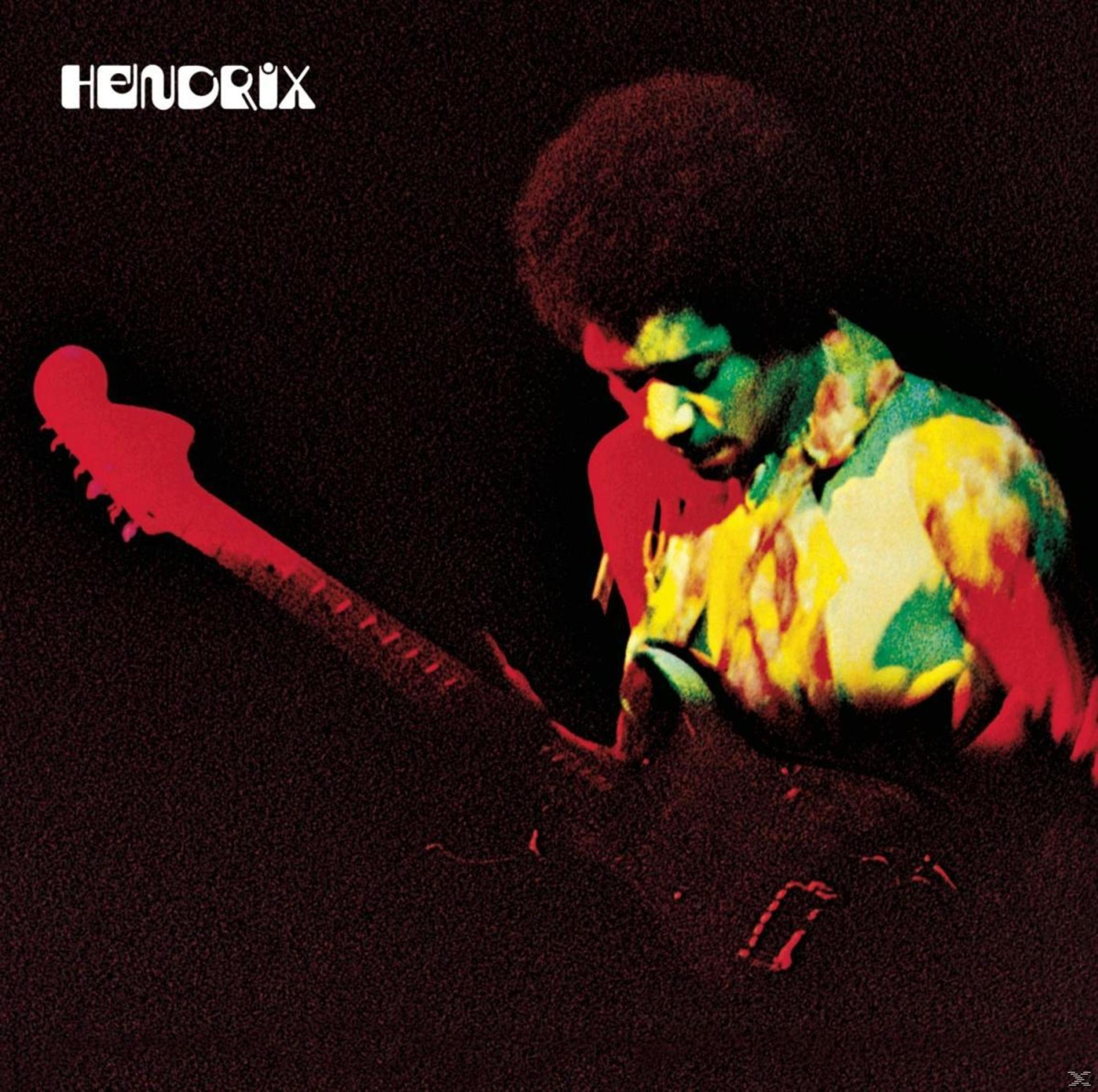 Jimi Hendrix suona la chitarra, camicia colorata, sfondo scuro, parola 'HENDRIX'.