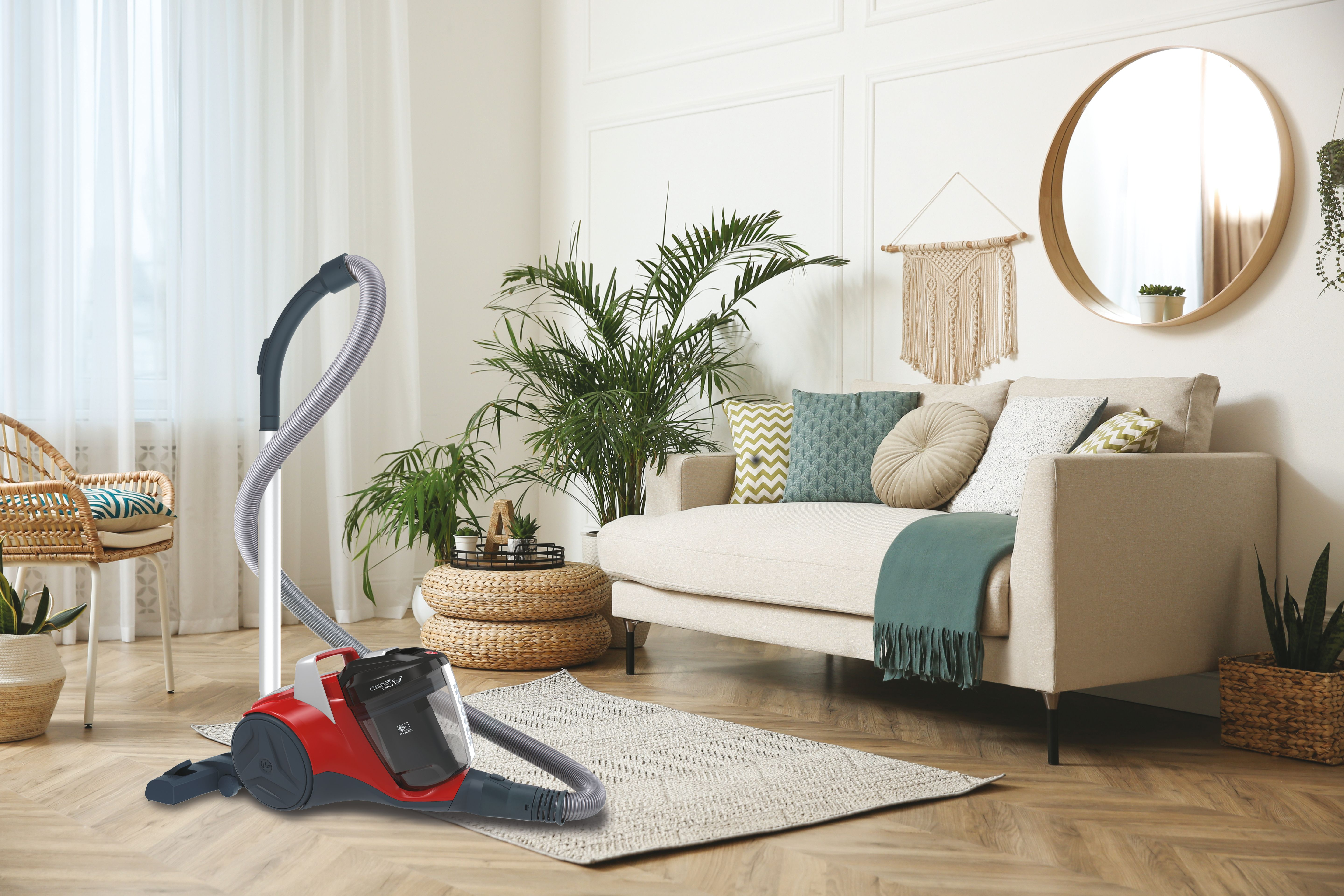 Salon z czerwonym odkurzaczem Hoover. Sofa, dywan, rośliny i lustro, tworzące domową scenę.