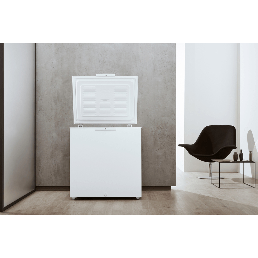 Congelatore a pozzetto bianco con coperchio aperto in una stanza con mobili.