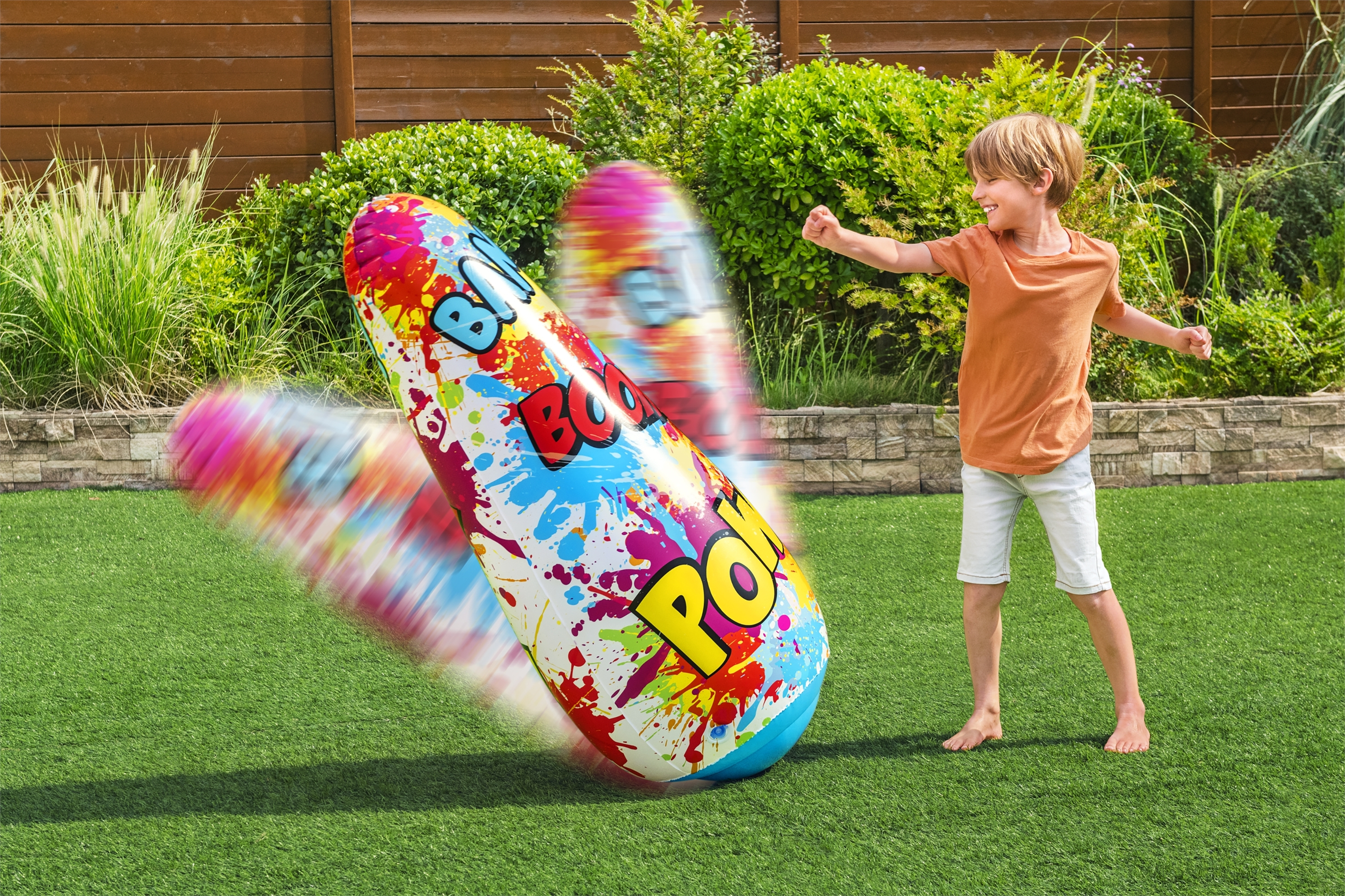 Un niño pequeño jugando con un saco de boxeo inflable en un césped verde.