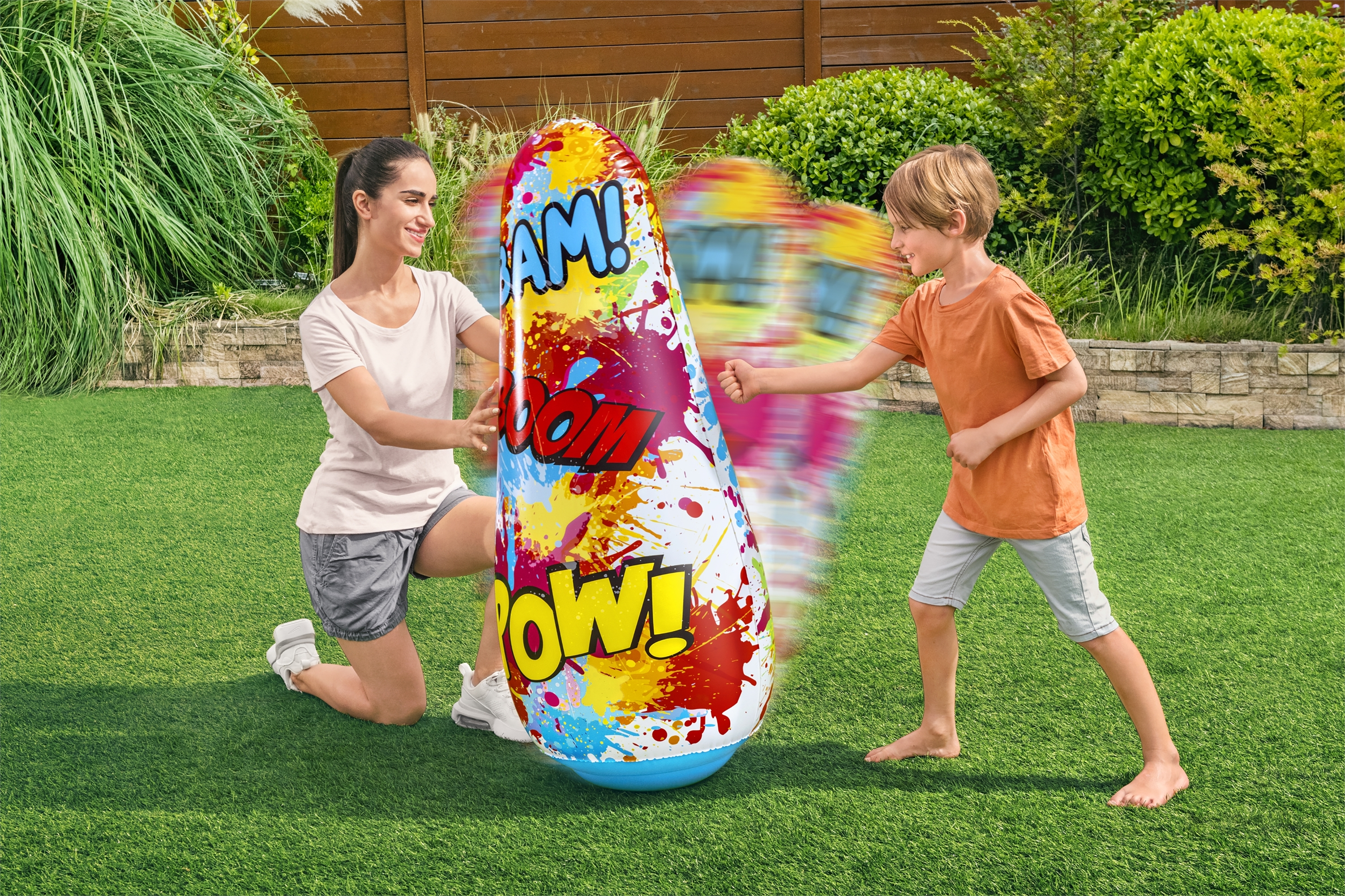 Una mujer y un niño juegan al aire libre con un saco de boxeo inflable y colorido.