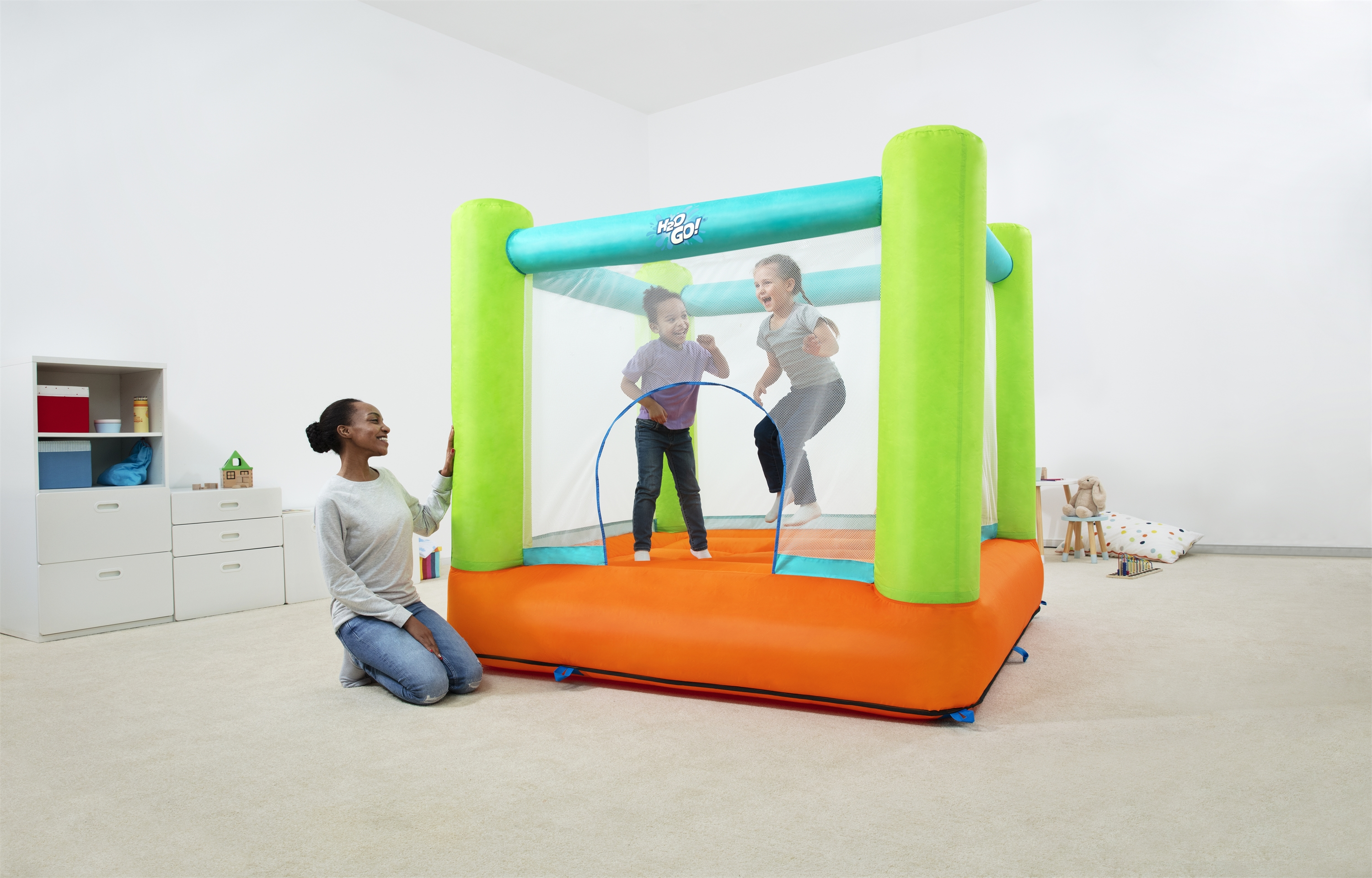 Dos niños saltando en un castillo hinchable, con una mujer observando cerca.