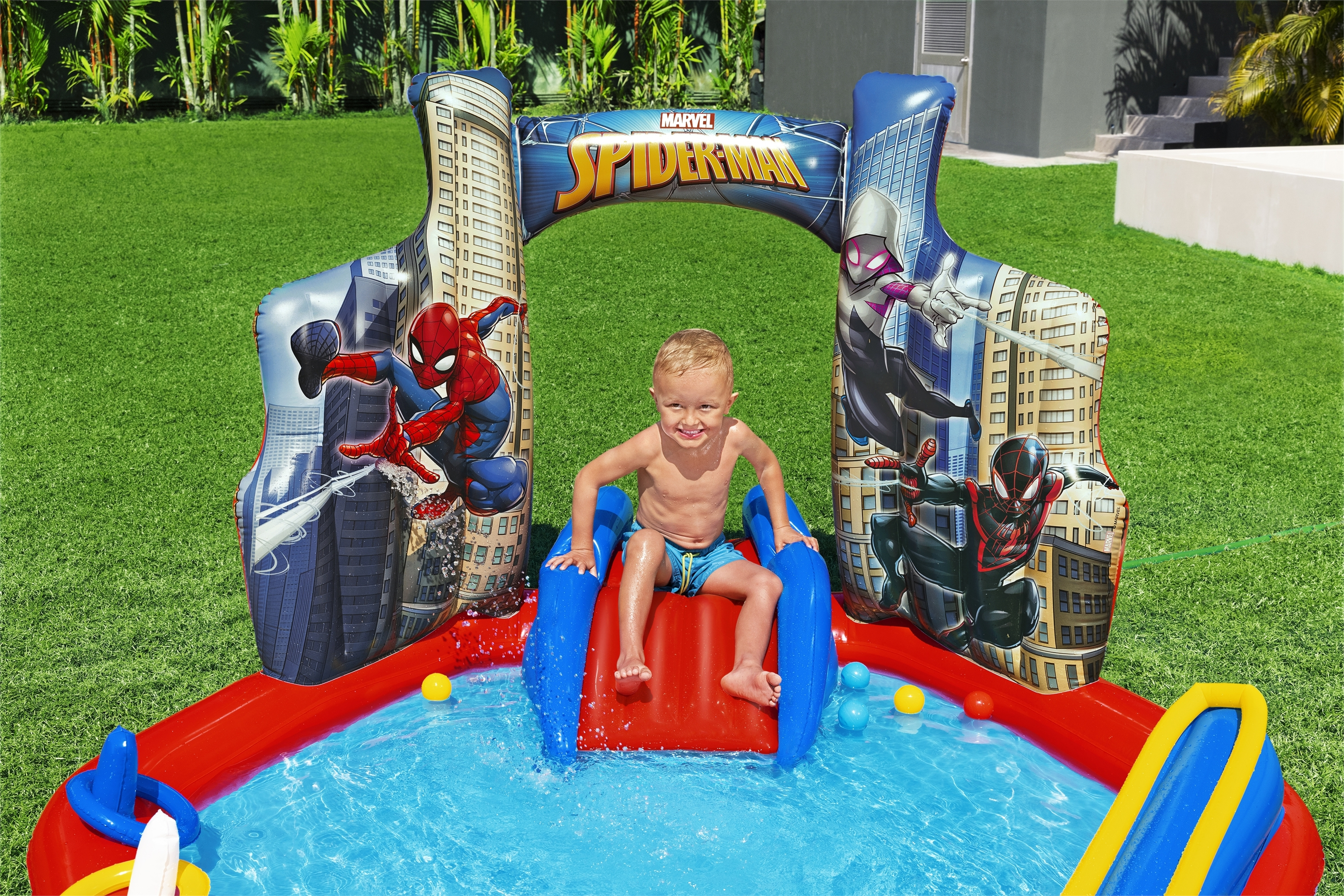 Dziecko w basenie Spider-Man z grafiką Spider-Mana, na zielonej trawie.
