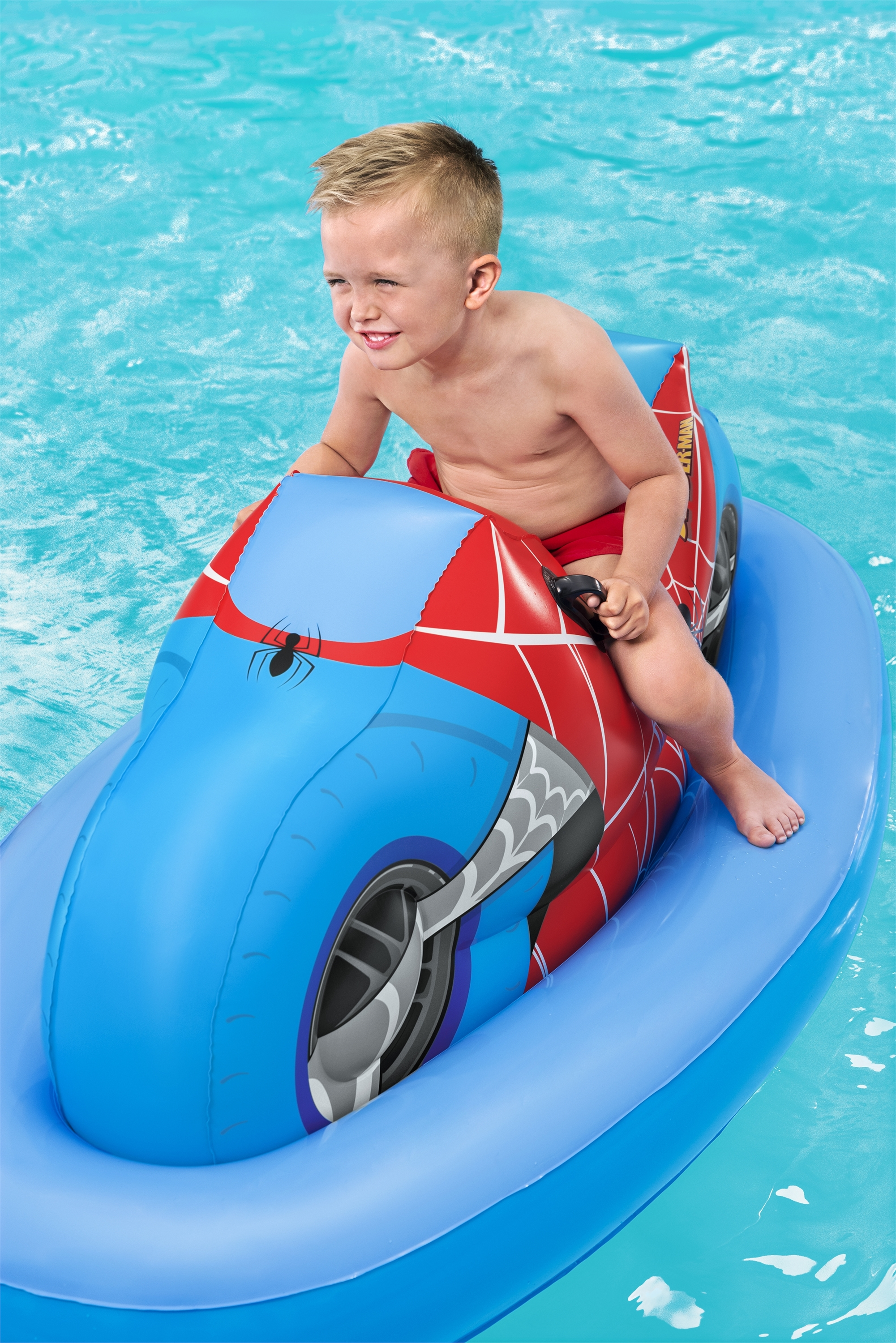 Ein Junge sitzt auf einem aufblasbaren Jet-Ski im Spider-Man-Design in einem Pool und lächelt.